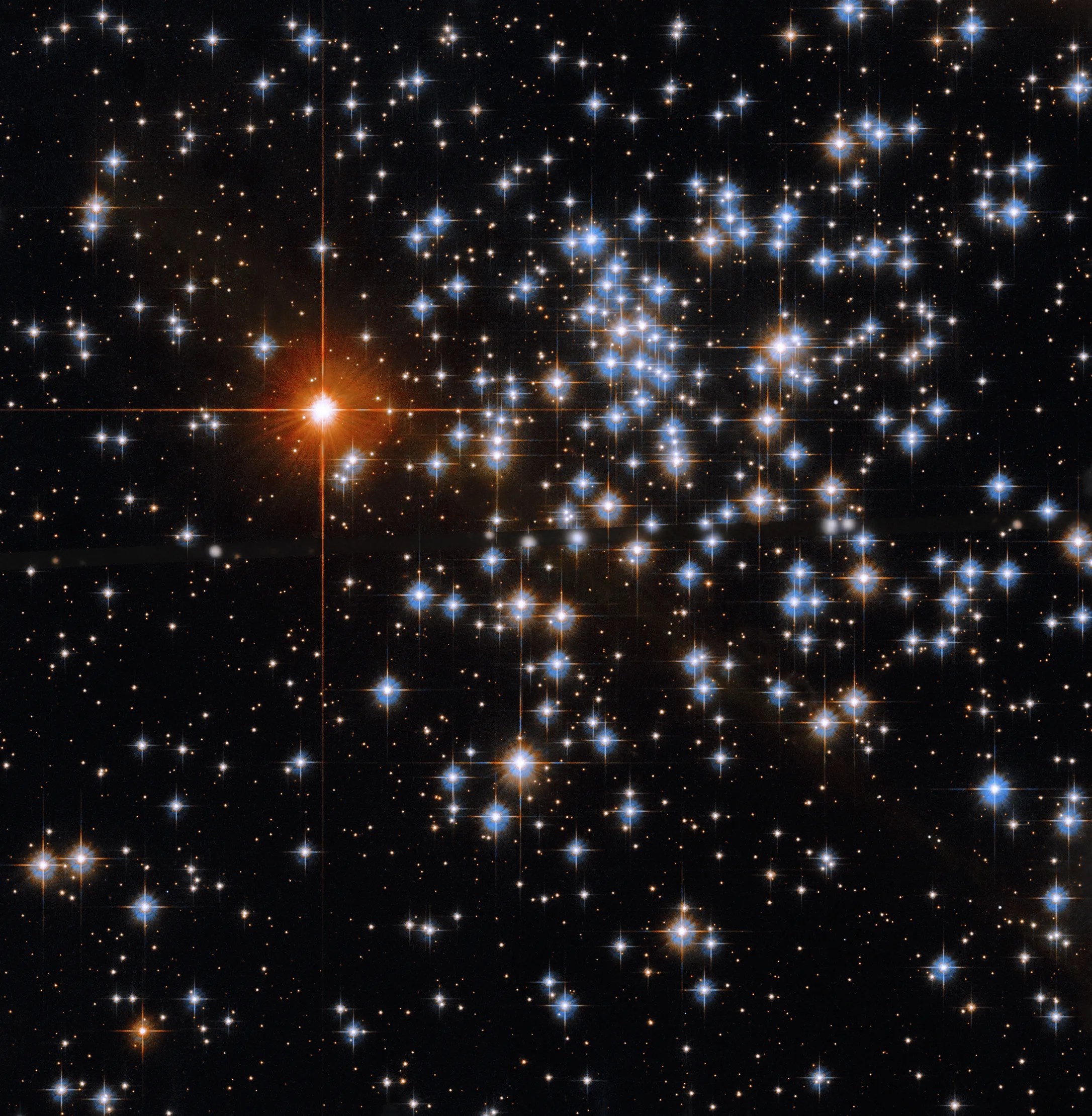 Bright blue-white stars fill the scene, but are concentrated on the right side of the image. a bright reddish-orange star sits in the upper left quadrant of the image near image center.