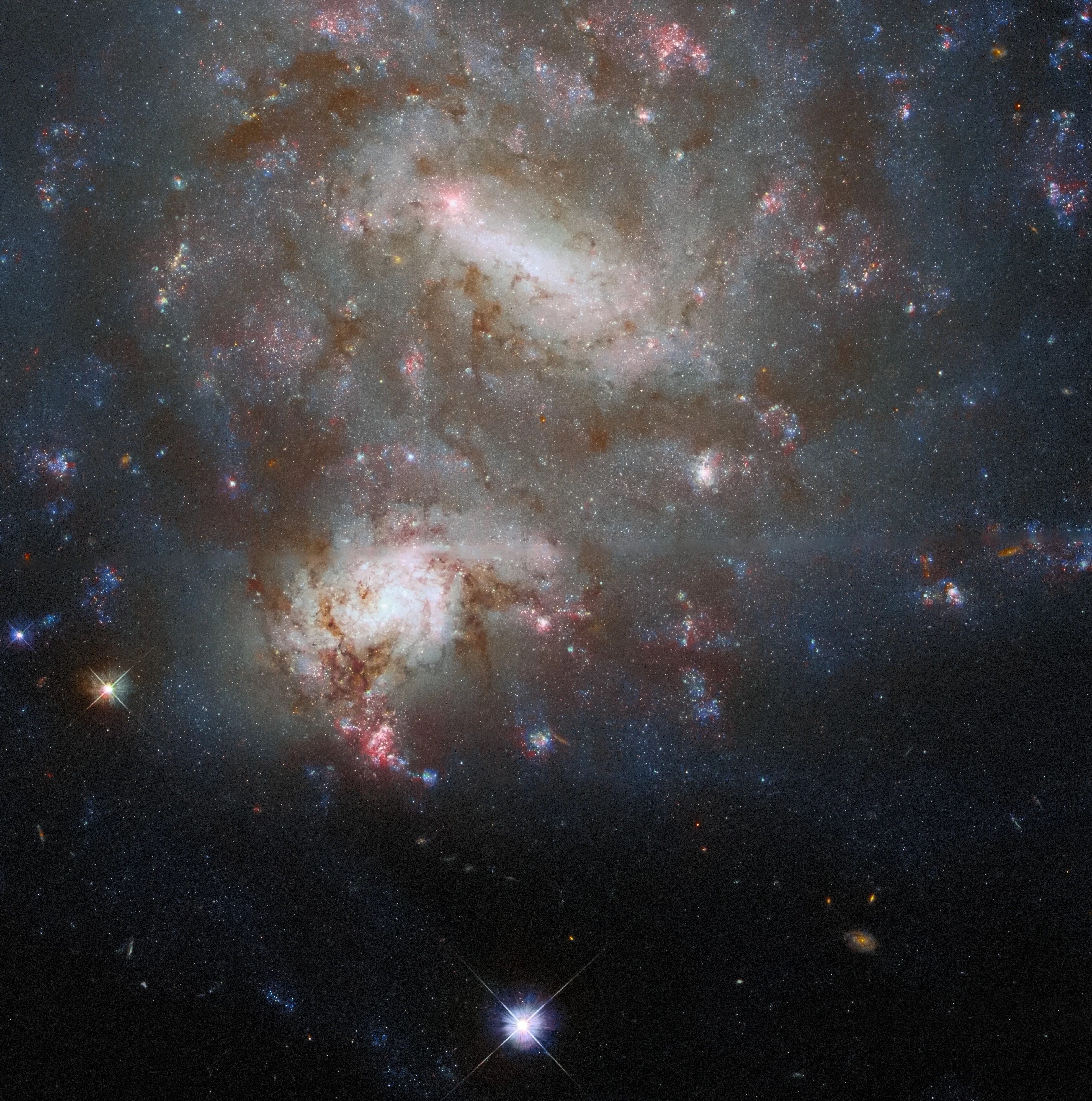 2 bright galaxies fill the top 2 thirds of the image. the larger one fills half of the image both have dark dust lanes and bright reddish-pink star-forming regions