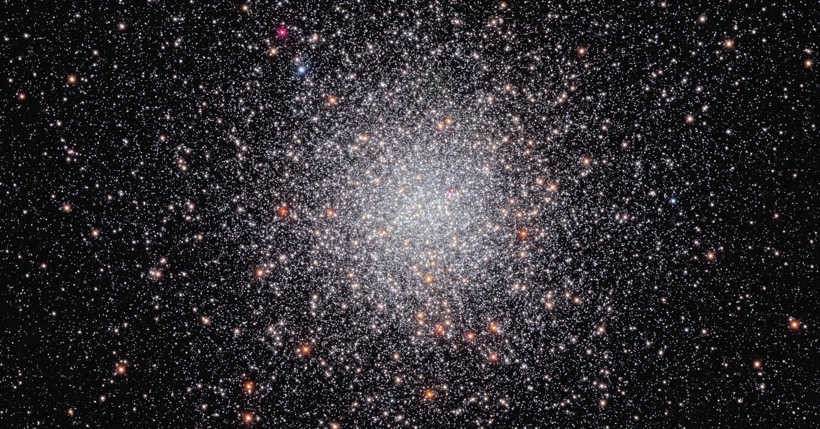 Center of the image is filled with a sphere of white stars. a smattering of orang-white stars dots the sphere. they are set against a black background that holds a smattering of stars.