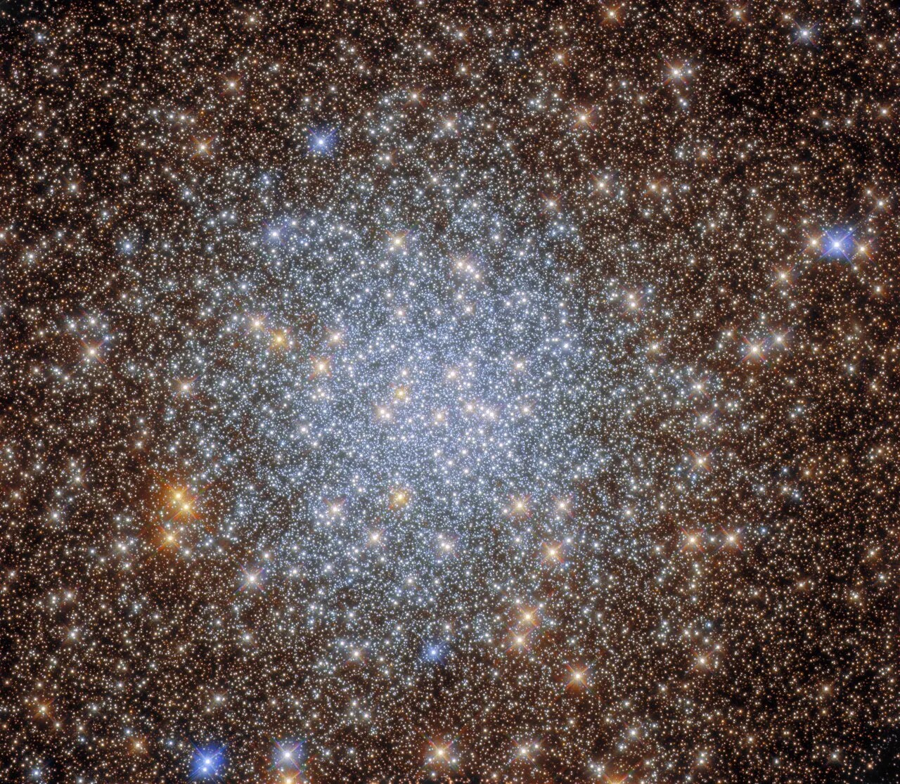 Stars fill the image; center holds sphere of densely packed, bright, blue-white stars; gold-colored stars, with a smattering of blue stars, surround the central sphere