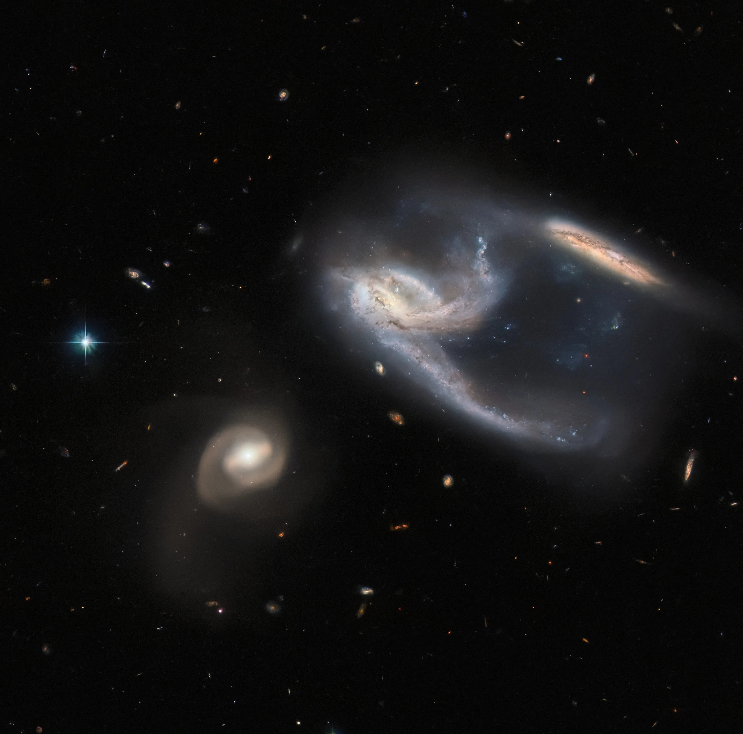 Three  galaxies, the center one holds two extended arms, one of which appears to connect to a galaxy at upper right.