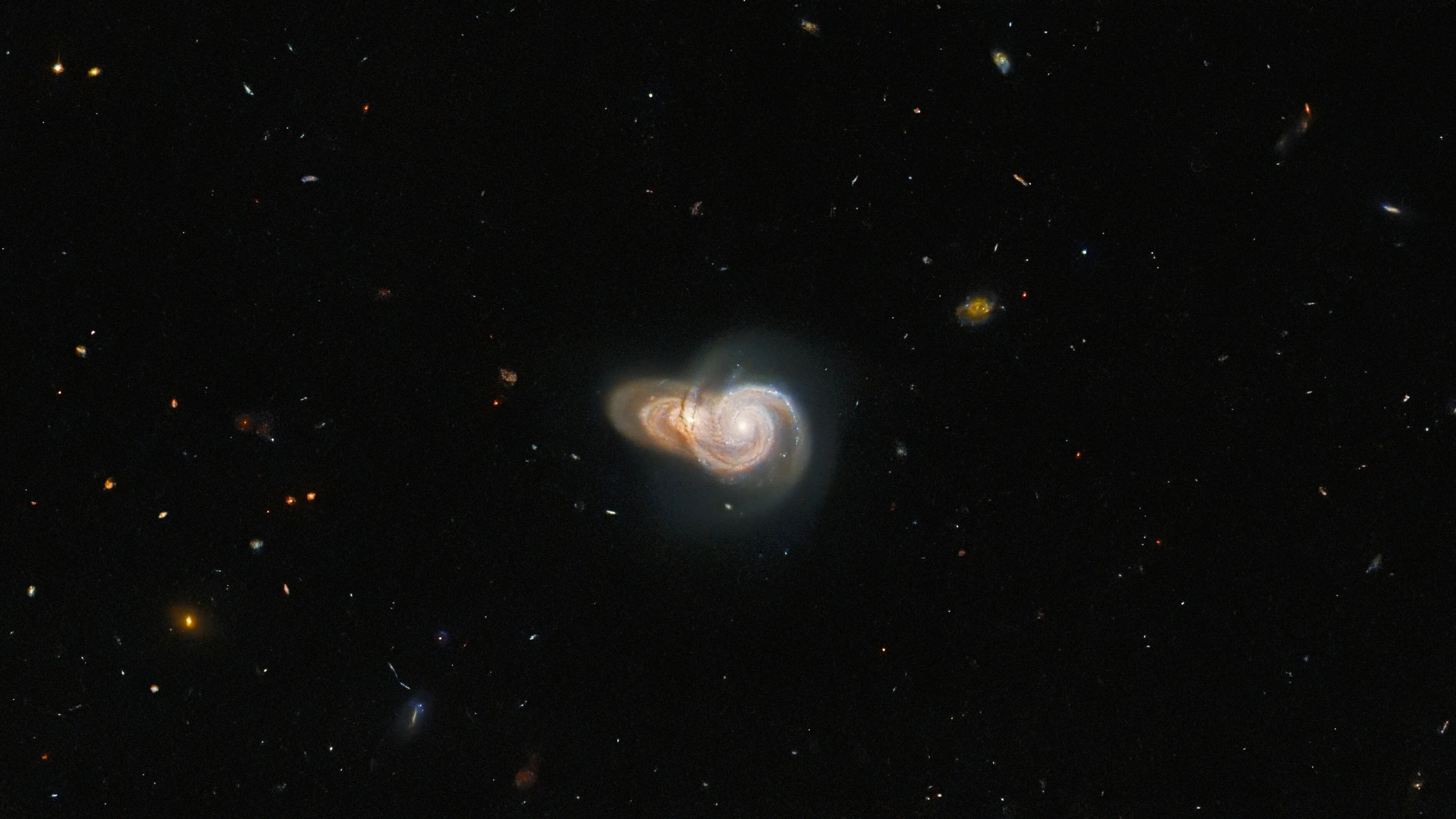 Center of image holds two spiral galaxies. the foreground galaxy is face-on, while the one behind it is at a slight angle. both appear yellow-gold with streams of bright white stars.