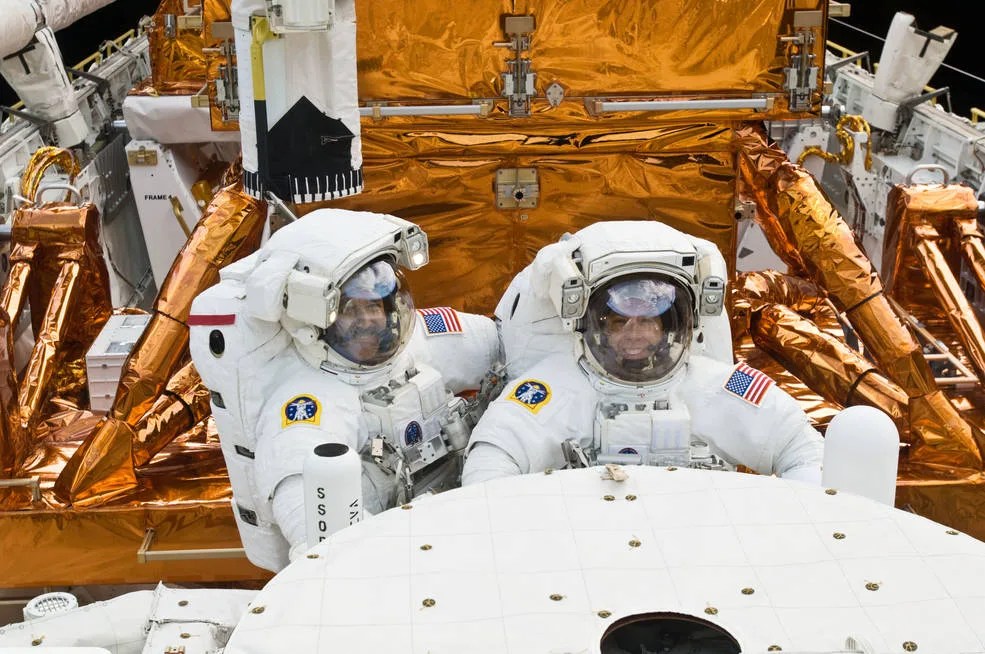 Two astronauts pose in front of Hubble in the shuttle cargo bay. They are both smiling broadly through their helmets.