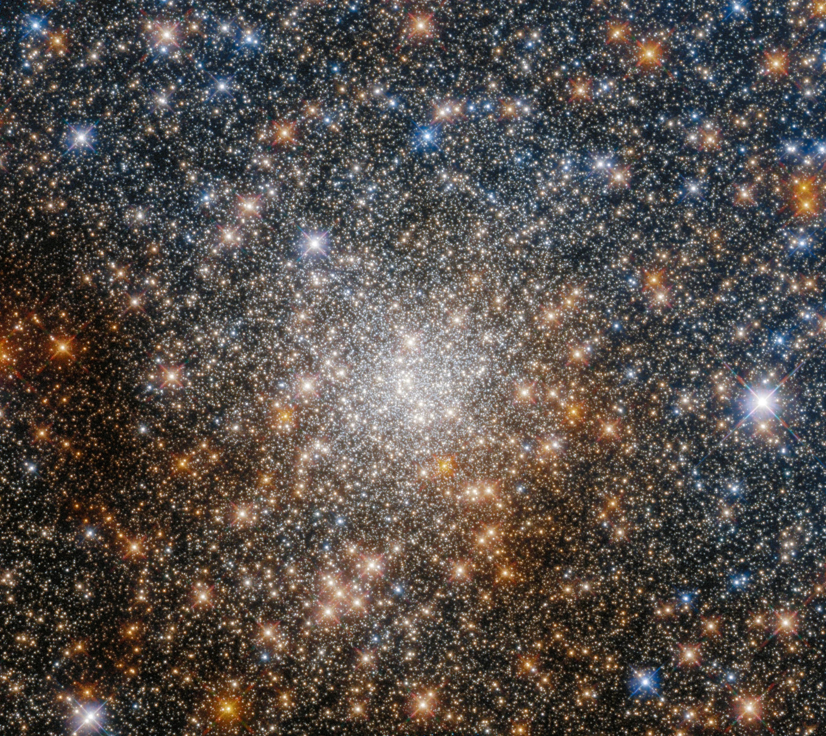 Bright-white stars dot the entire scene but are concentrated at the center of the image. gold stars dot periphery with more filling the bottom half of the image. a smattering of blue-white stars with most in the upper half of the image.