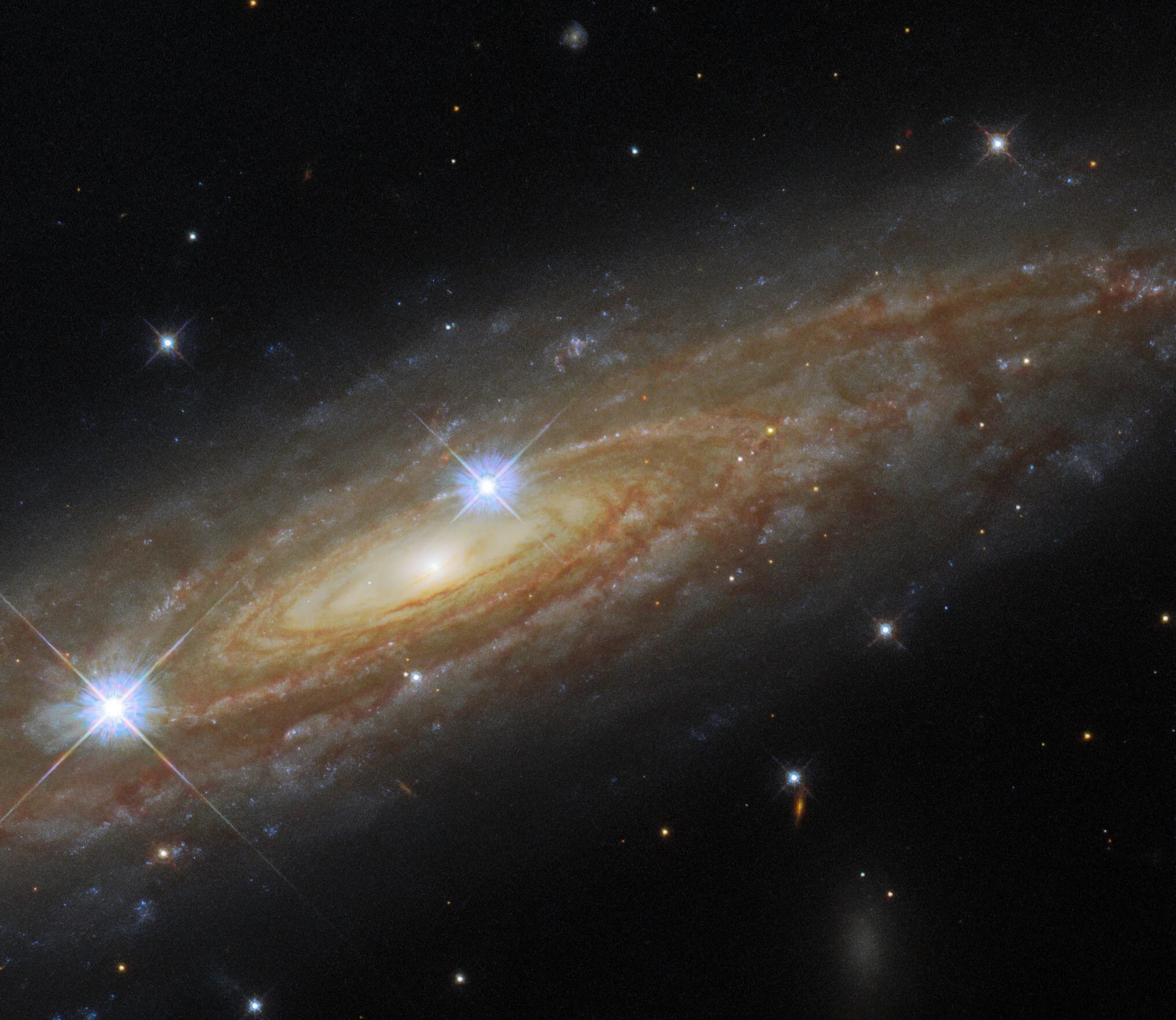 Spiral galaxy stretches from lower left to upper right of the image. two bright foreground stars are also in the image.