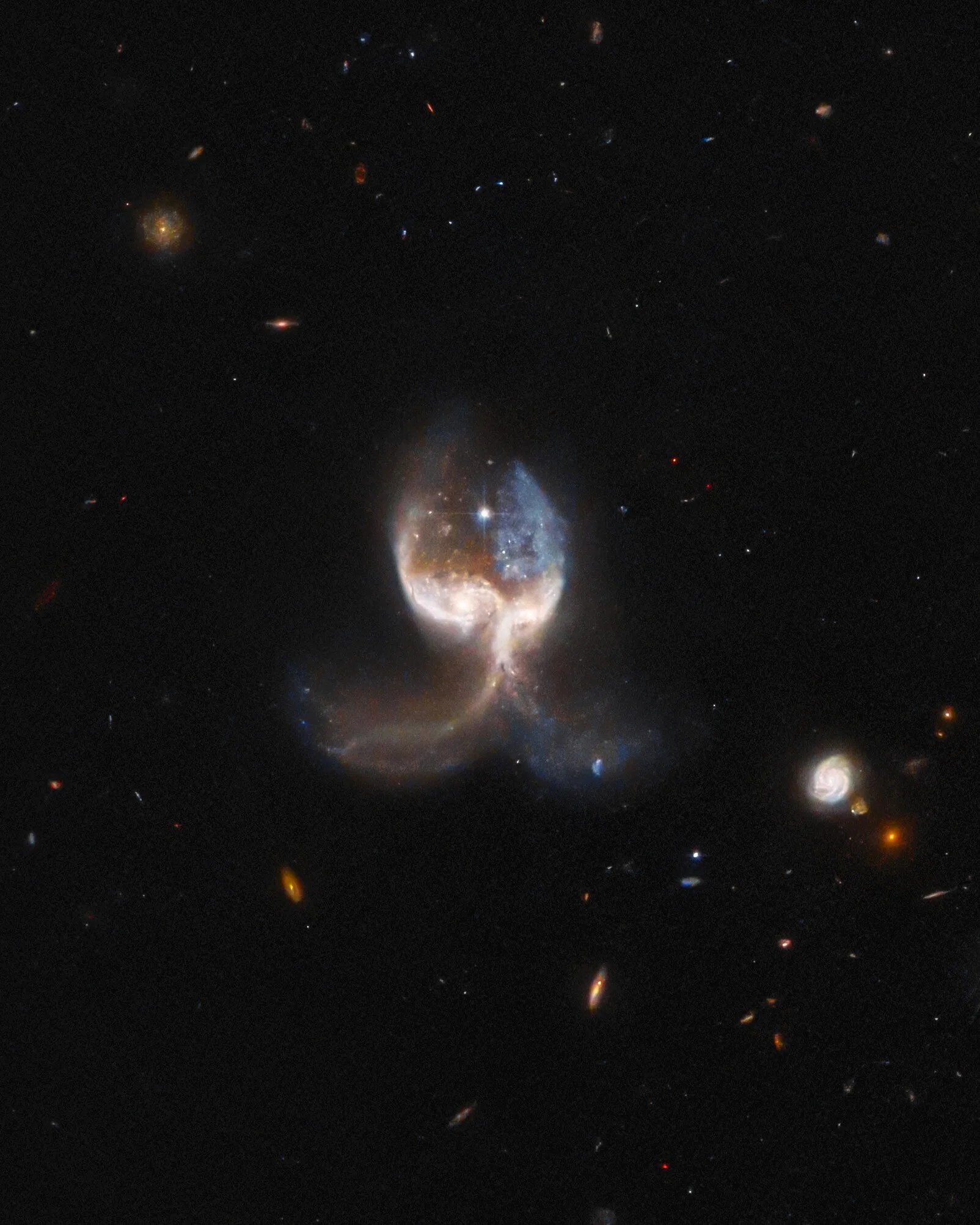 2 merging galaxies at image center form what looks like an angel with large wings. distant galaxies dot the background