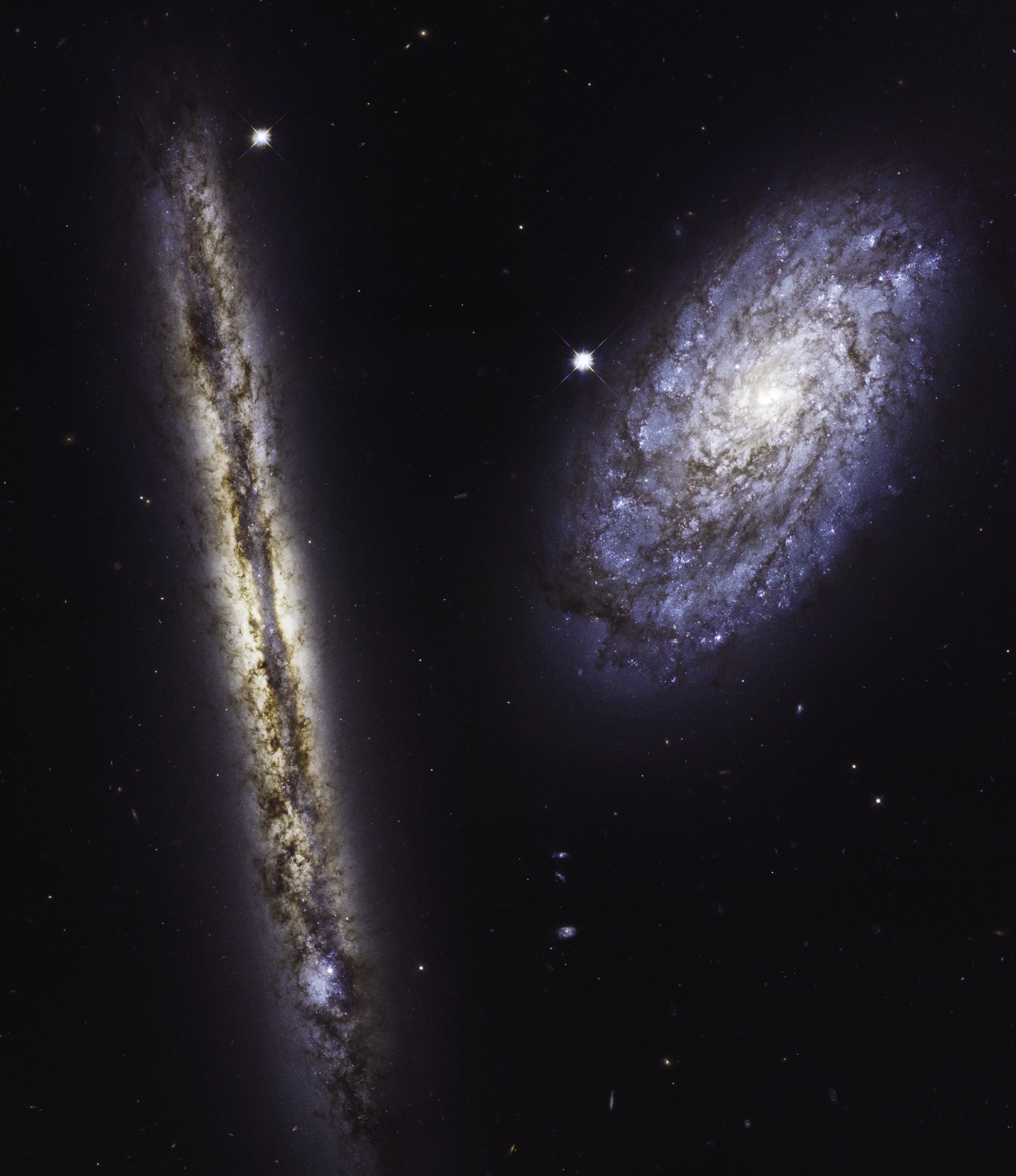 Two spiral galaxies are viewed against black space. One is facing us, while the other is viewed edge-on.