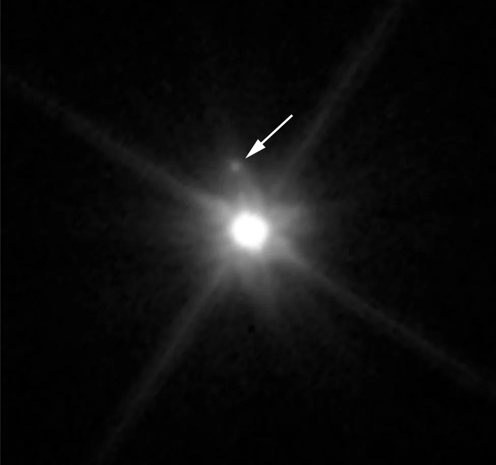 Hubble's view of Makemake. Bright-white Pluto is at the center of the image. An arrow points to a small white dot just above the planet.