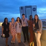 Six young adults standing for a posed photo on a balcony at KSC overlooking the VAB