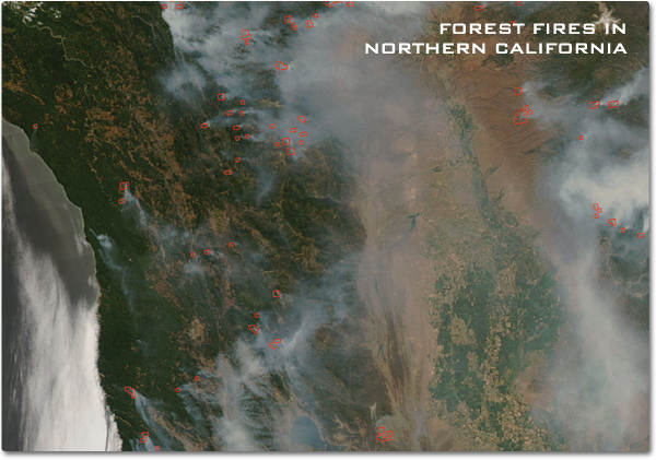 A satellite image showing smoke from forest fires wisping across the forest covered landscape of Northern California. Bright red areas at the base of these smoke plumes indicates the size of the actual area on fire.