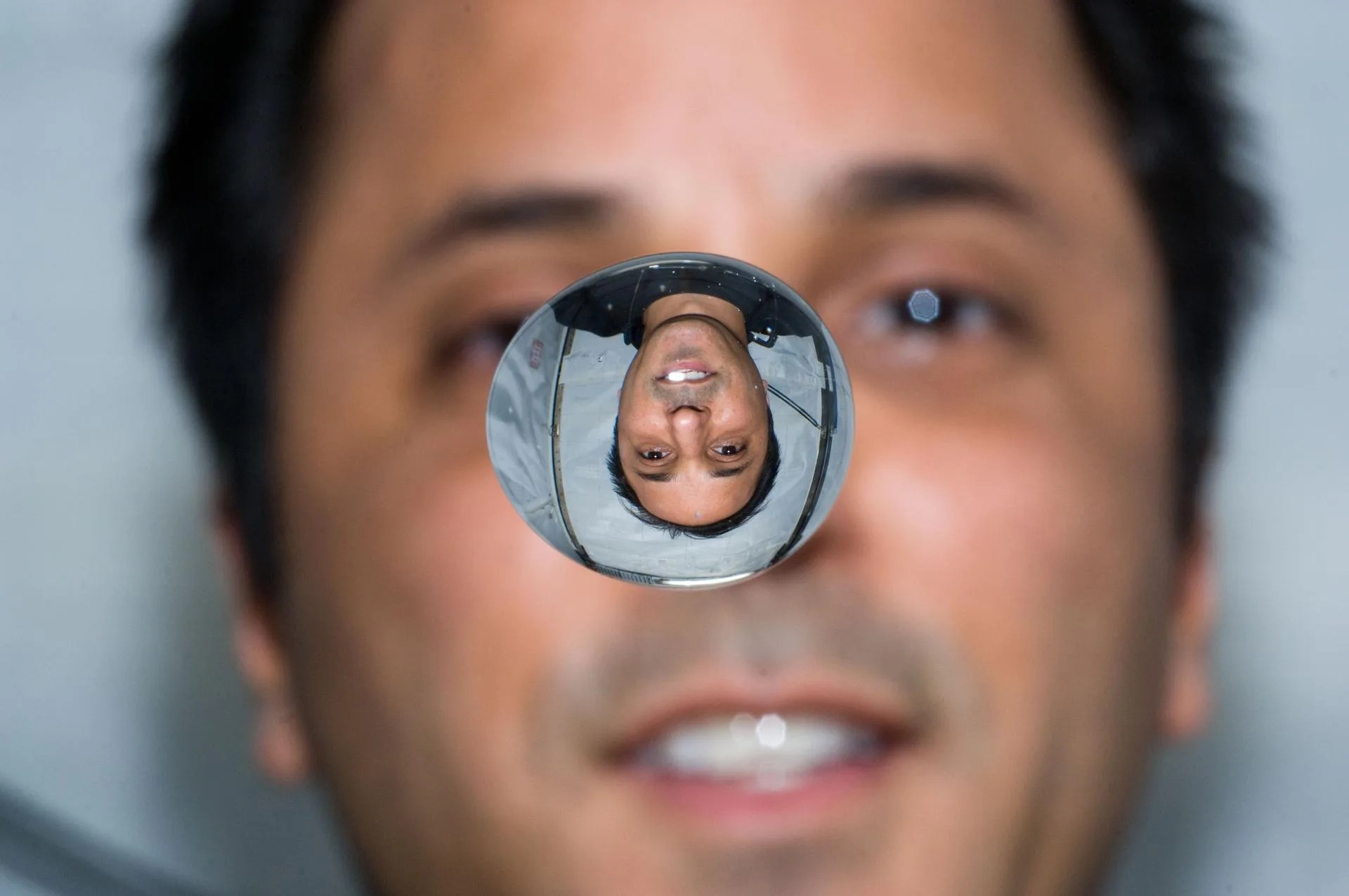 Man watches liquid bubble float in front of him, reflecting his face upside down.