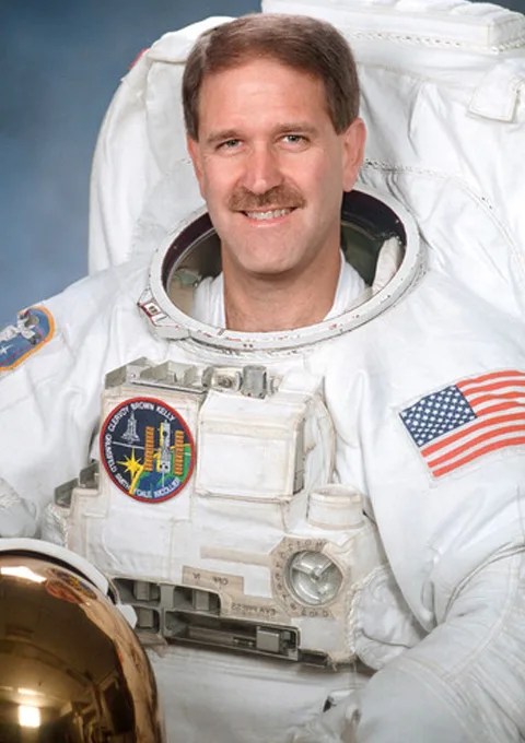 John Grunsfeld wearing an astronaut suit and holding his helmet.
