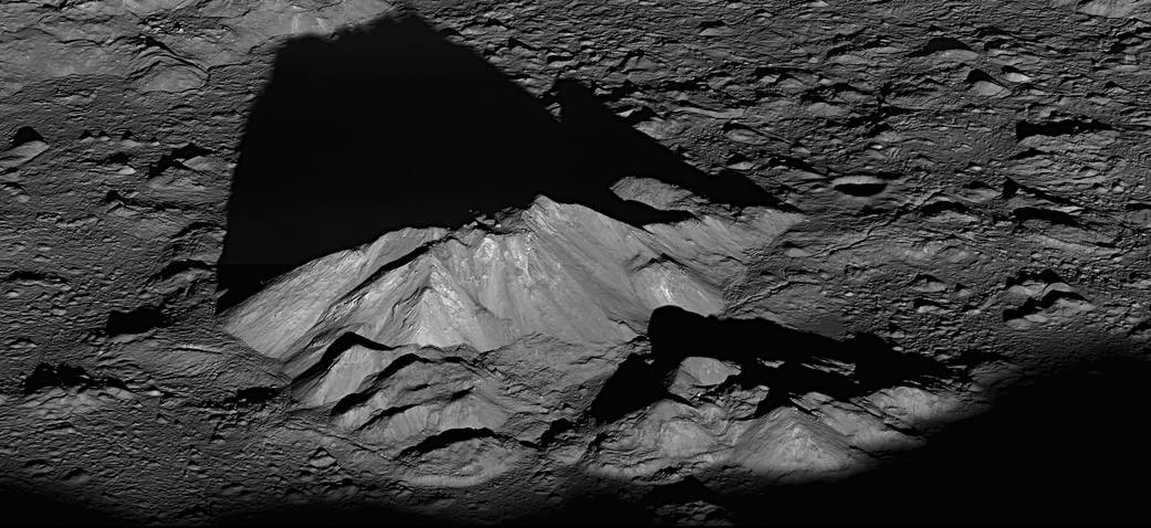 由月球岩石组成的山脊是灰色的，带有银色的亮点。一个巨大的黑暗阴影延伸到第谷中央山峰的后面。前景由较小的陨石坑丘组成，这些陨石坑同样受到阳光的照射。