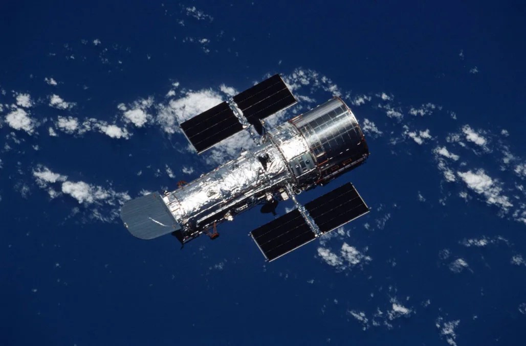 Hubble Space Telescope positioned over Earth with blue oceans and clouds in the background.