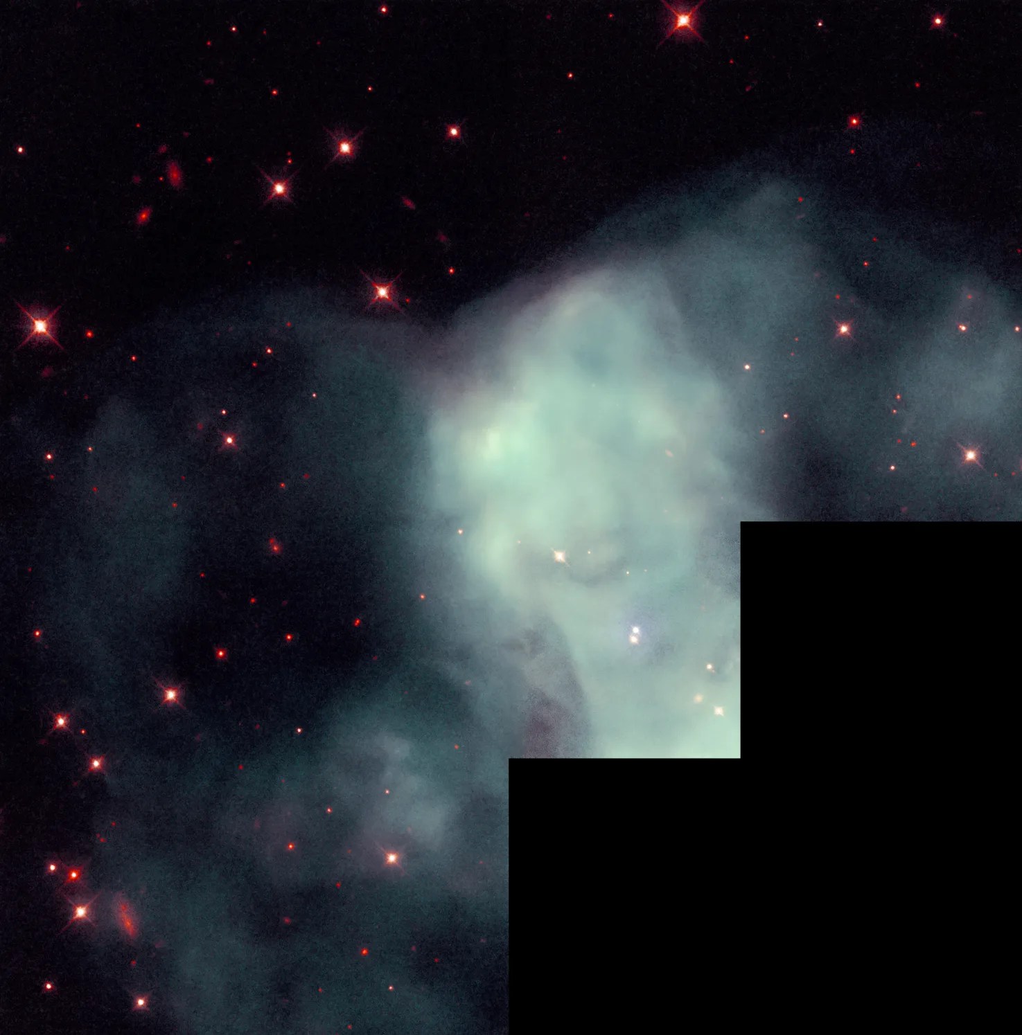 A hazy cloud of pale green covers the center of the image, against black space dotted with reddish stars. A stair step region of black at the lower right shows where there is no Hubble data.