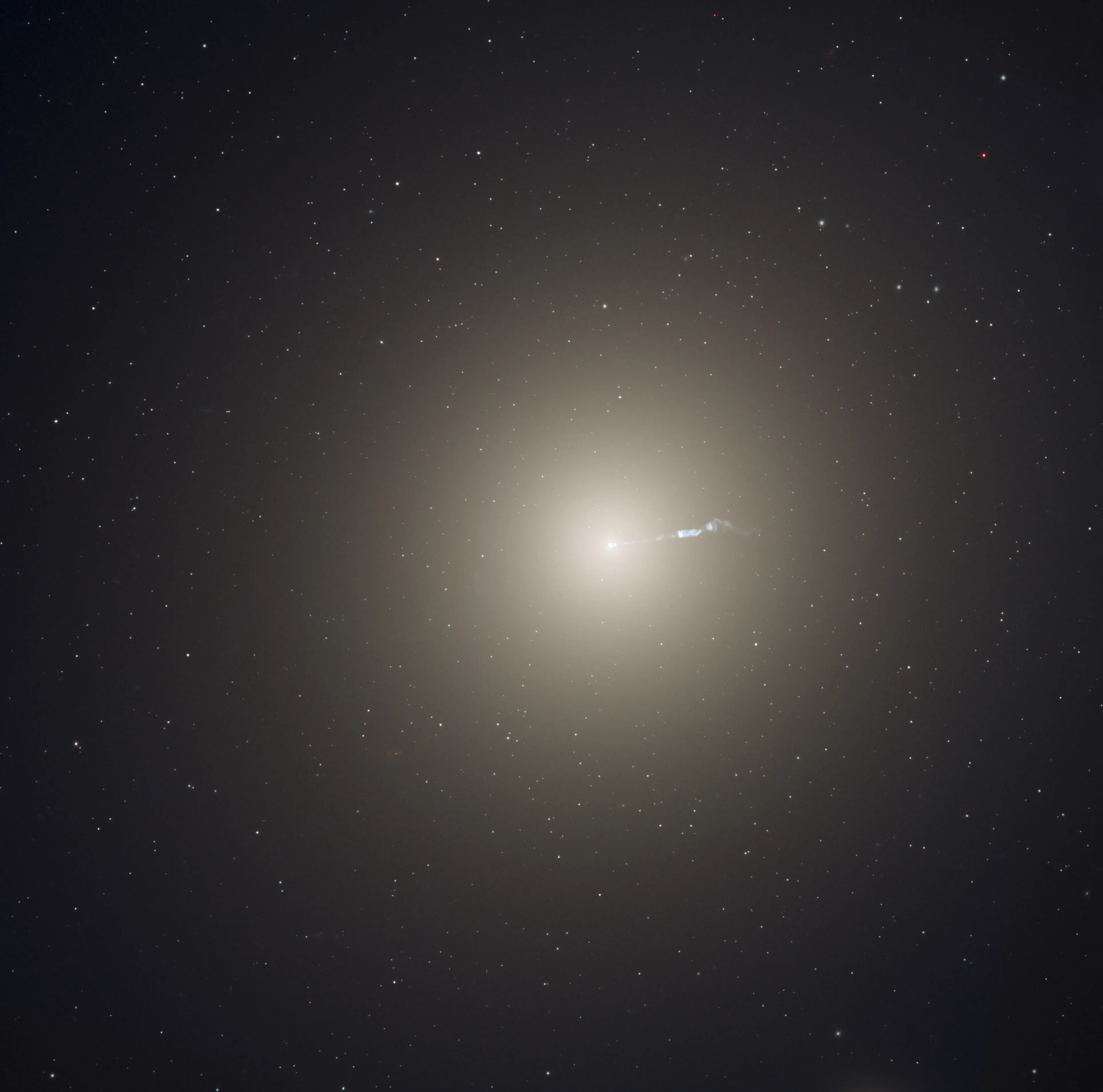 A bright, yellowish galaxy core shines near the center, with a faint jet of material ejecting toward the right.