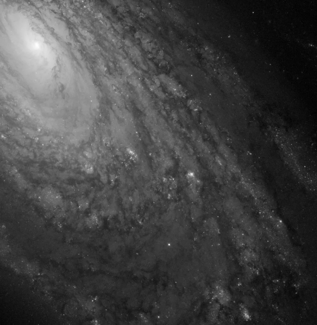 This image shows a bright galaxy core at the top right, surrounded by spiral arms, all in grayscale.