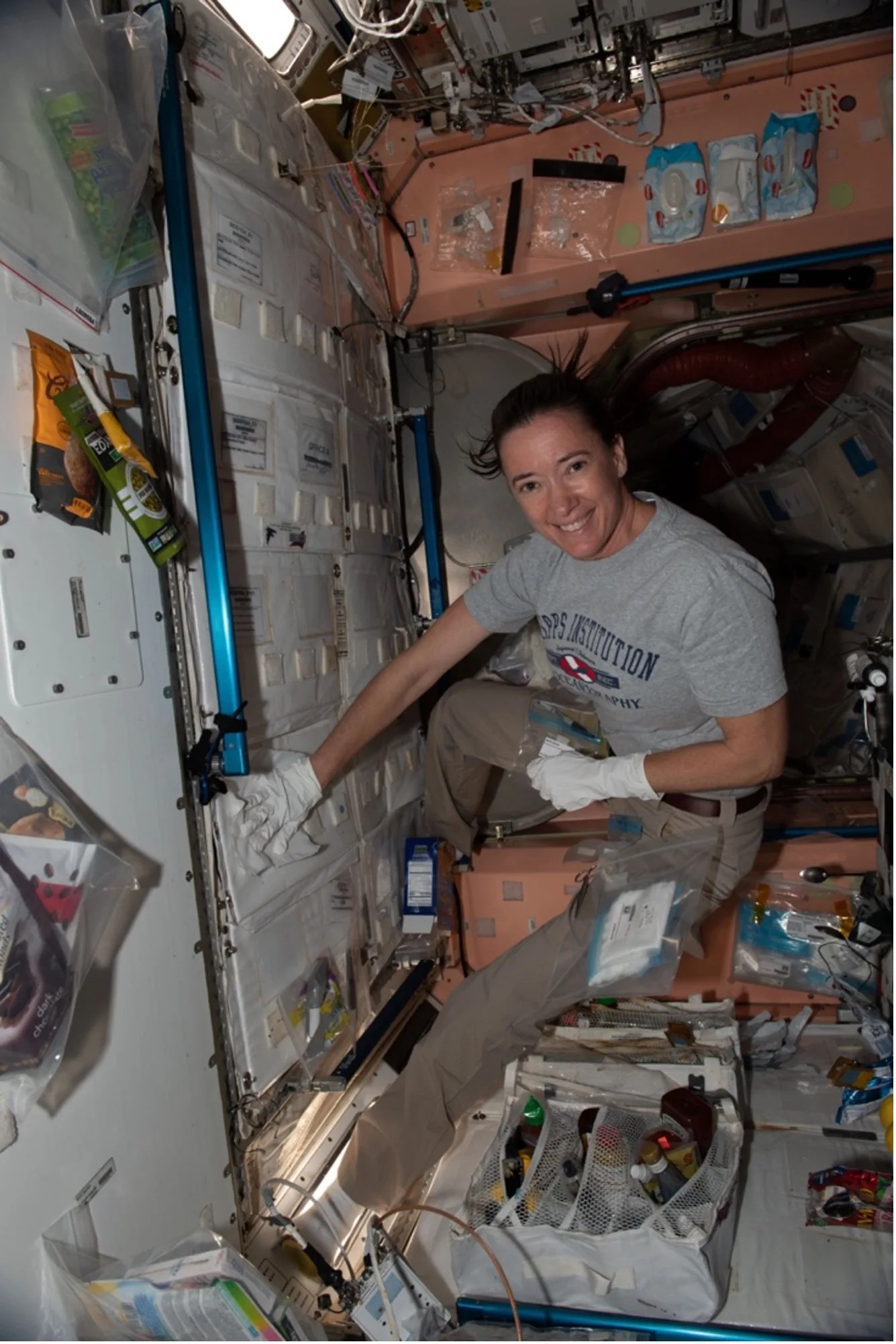 Weightless woman wearing white gloves taking samples from wall surface in the International Space Station.