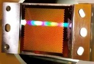 Photo of a rainbow pattern of diffracted visible light in front of a honeycomb pattern panel.
