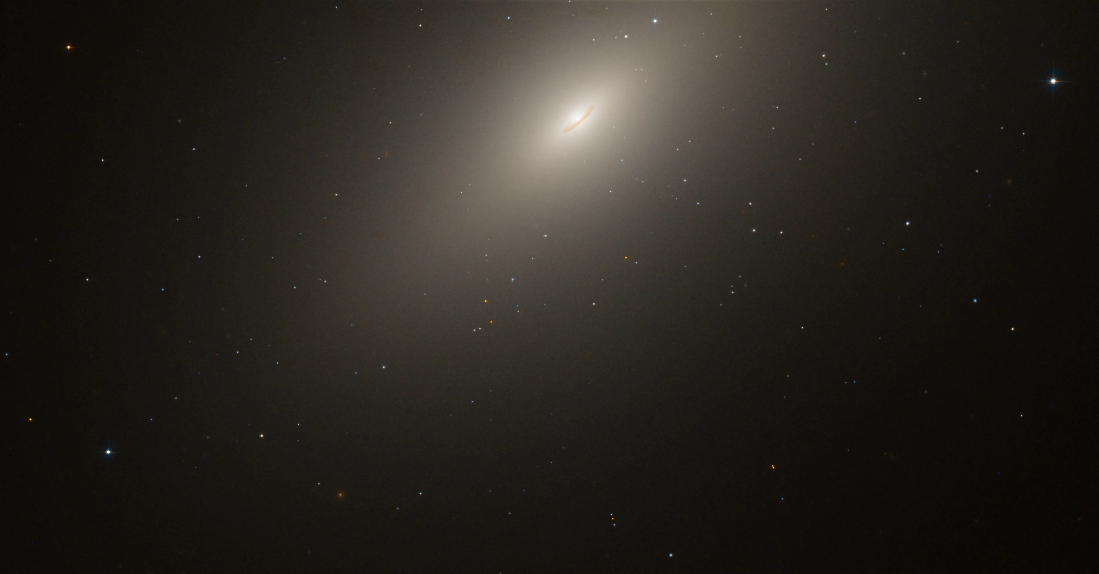An elliptical galaxy emits a bright white glow that surrounds it like a halo.