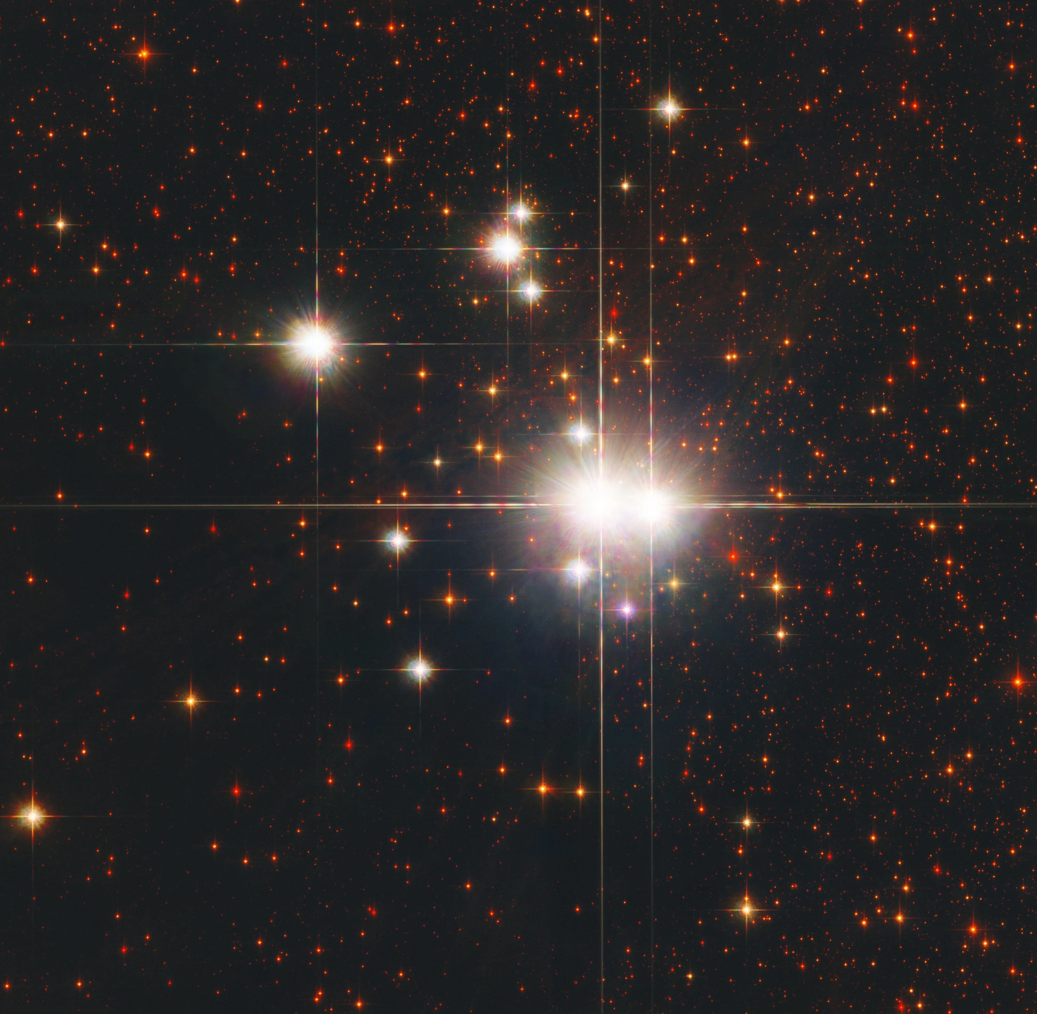 Several very bright whitish stars are clustered together, with a number of smaller and dimmer red stars around them.