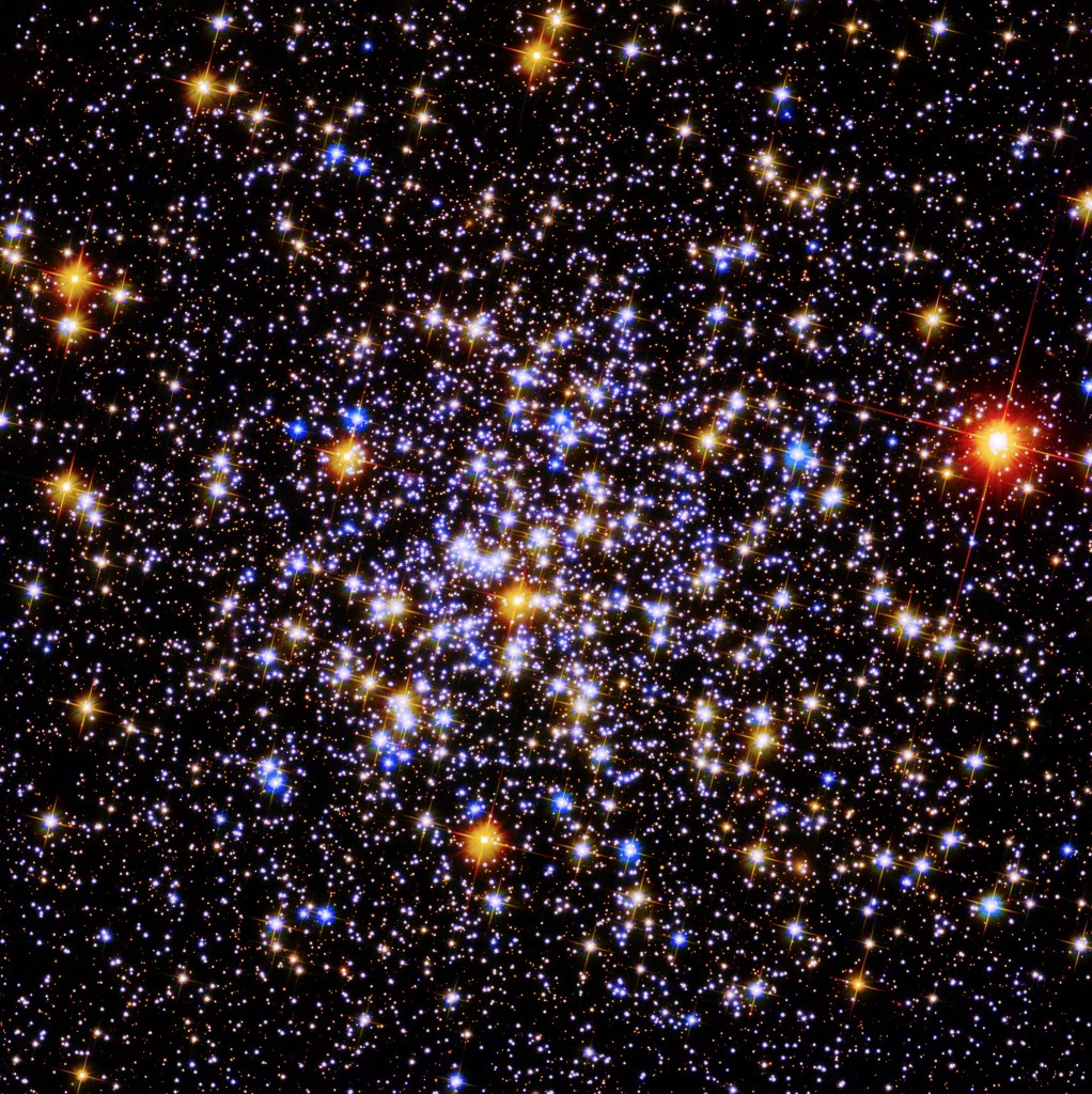 A cluster of bright blue and yellow stars against the black background of space. A single bright red star is to the far right.