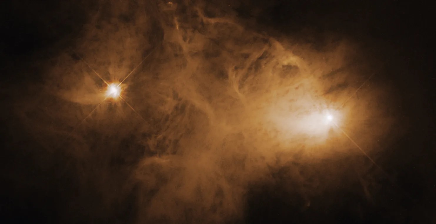 Two bright stars shine a distance away from each other, looking like eyes. An orangey haze emanates around and between them.