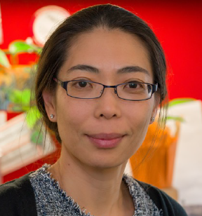 Portrait photo of a young smiling woman with long dark hair pulled back and eyeglasses; the backdrop is red and colorful