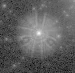 Grey, black, and white image. At image center is a star with a haze surrounding it. The haze holds brighter lines that appear to radial spread bisect the haze at regular intervals.