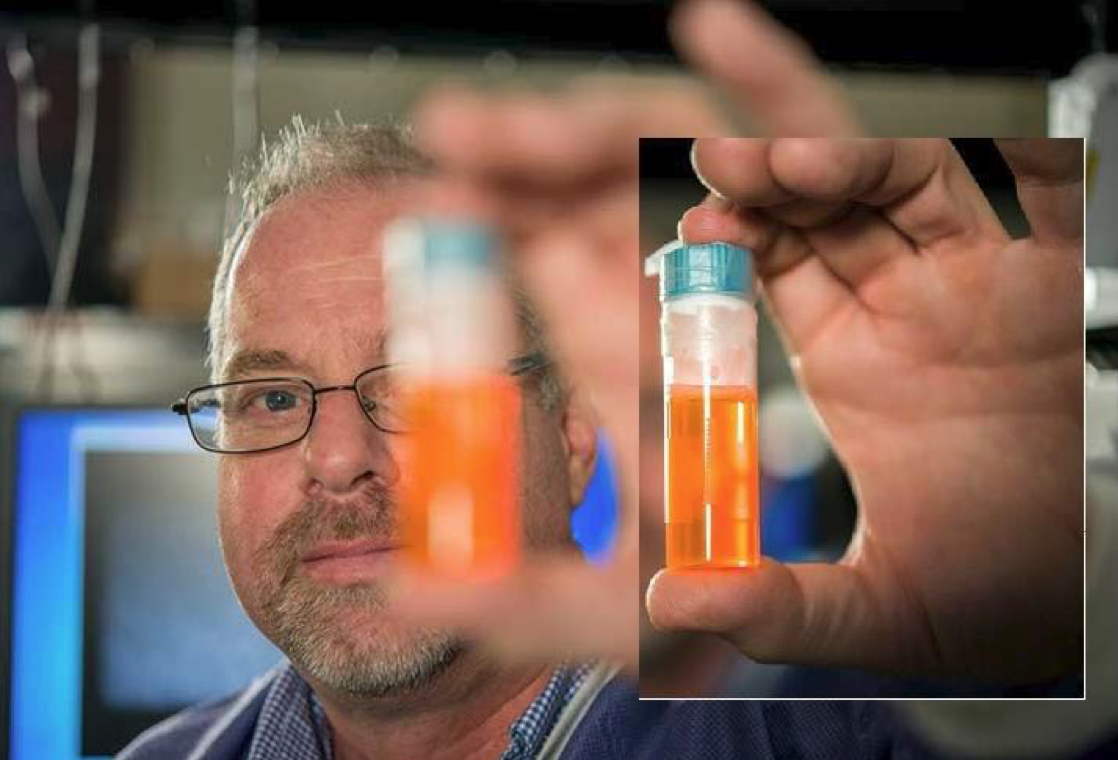 Man holds small tube of orange fluid