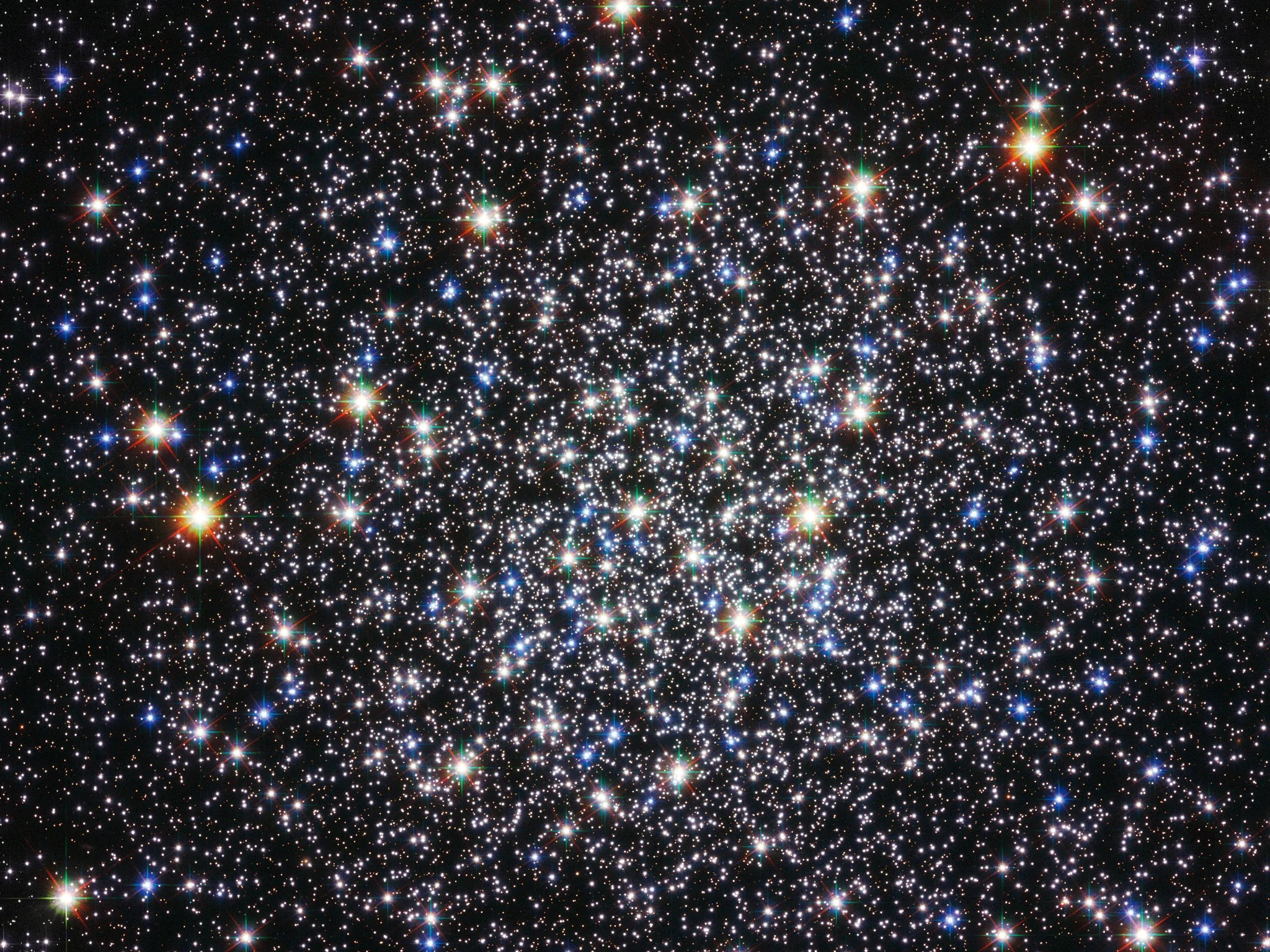A globular cluster of thousands of white, blue, and larger yellow stars.