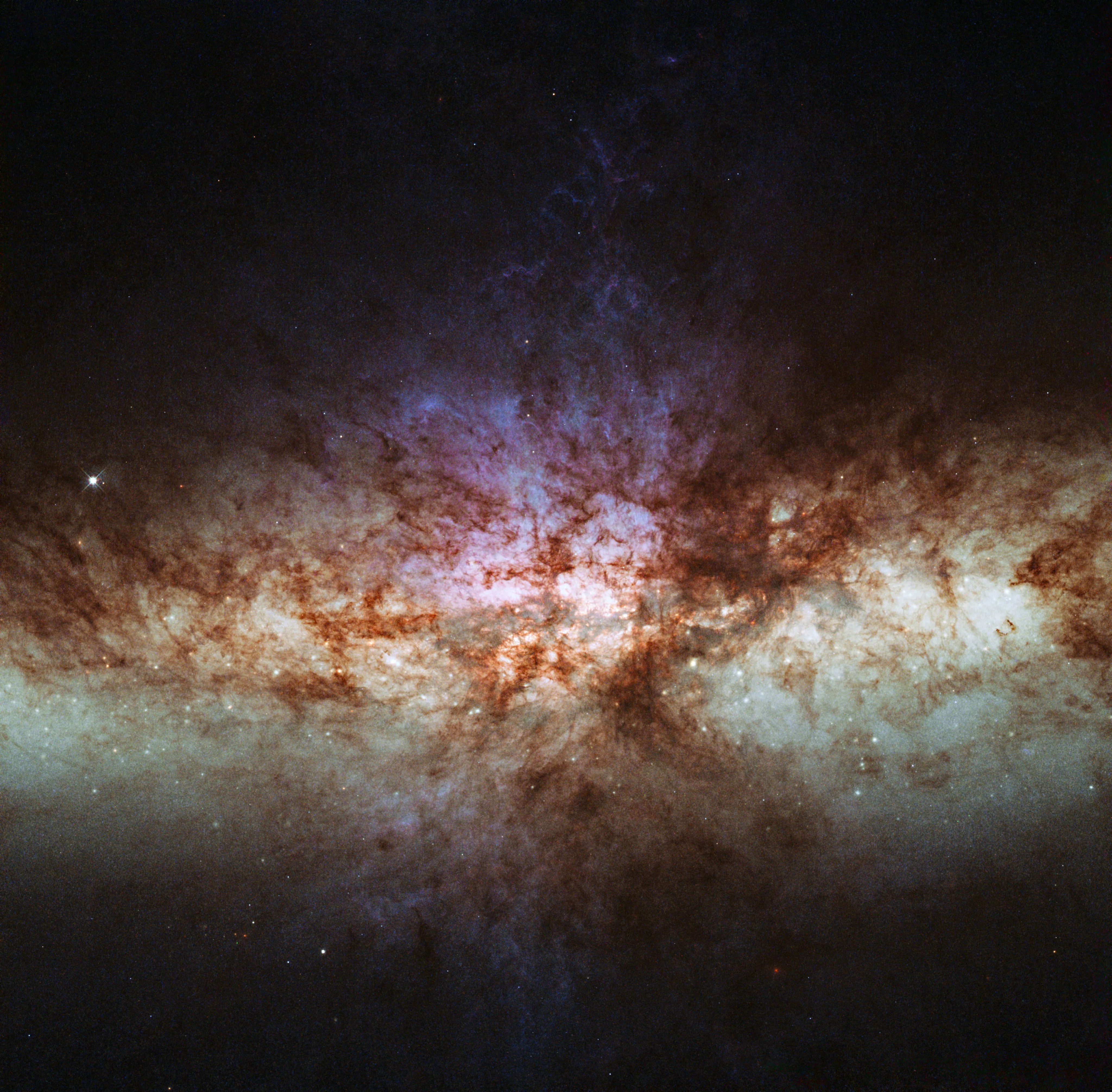 A bright glowing region in pale green and purple stretches across the image, laced through with dark brown lanes of dust and black space along the top and bottom.