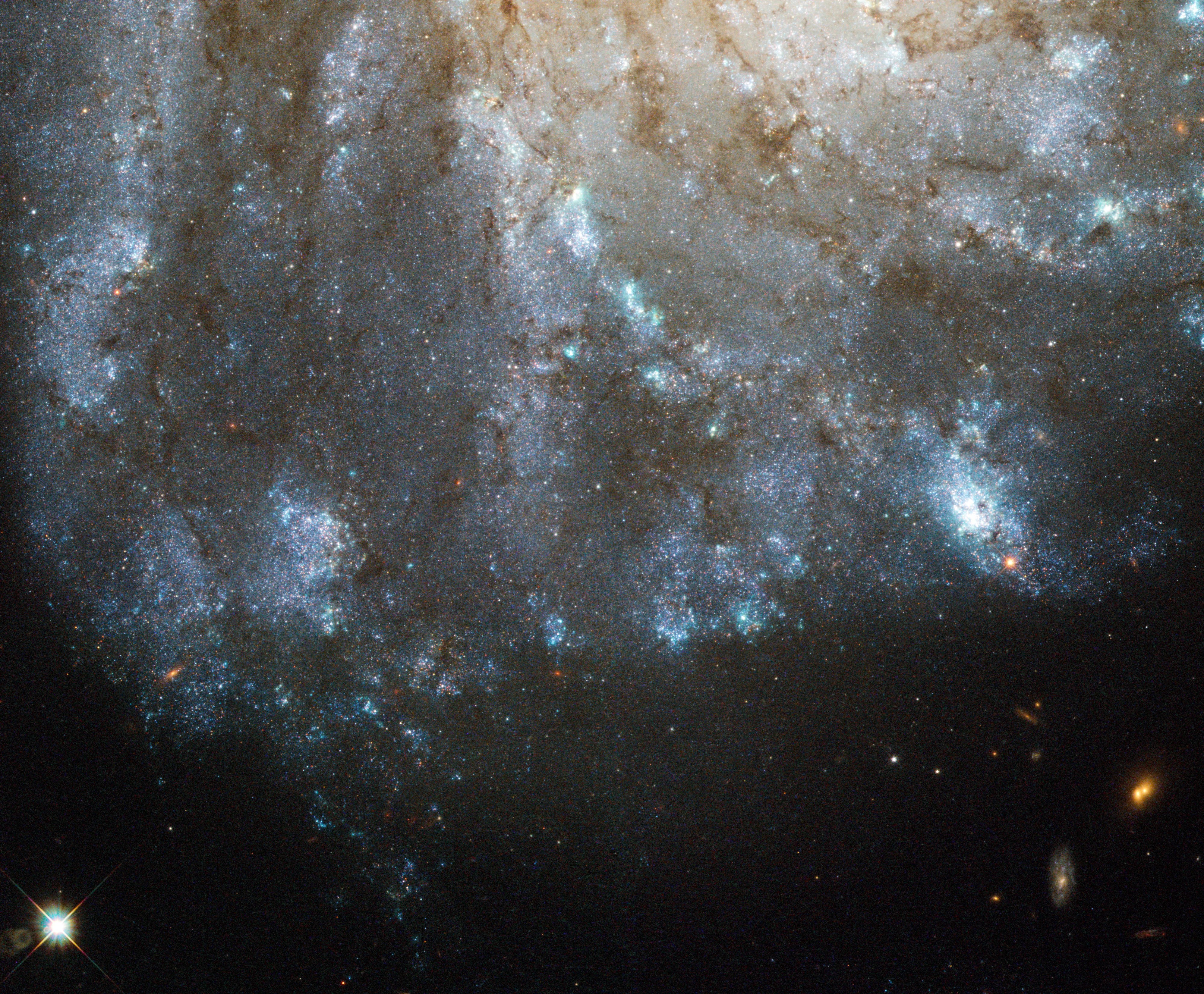 The bright blue spiraling arms of a galaxy are seen against black space, with a yellowish core visible near the top of the image.