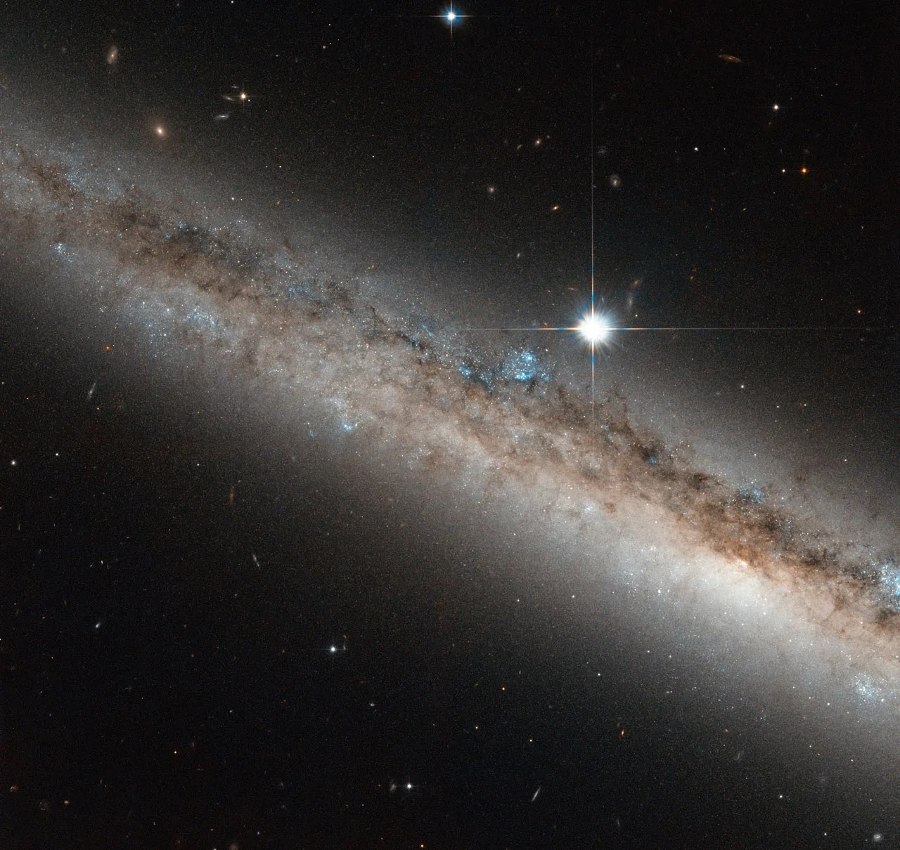 Edge on view of a galaxy angled down to the right, with a bright star above