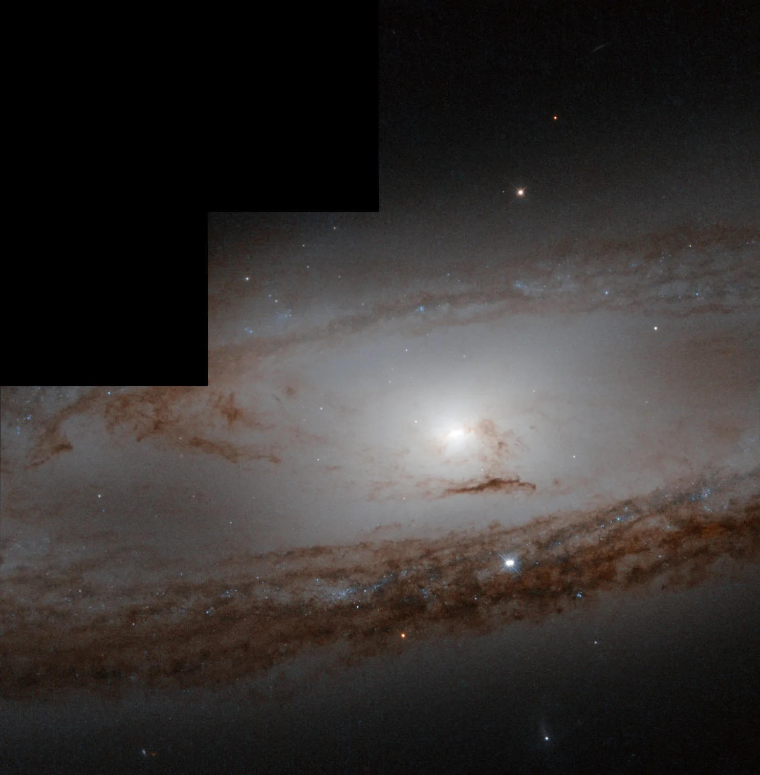 A spiral galaxy with a bright core fills the image, surrounded by faint spiral arms laced through with dark dust. A black rectangle is at the upper left, showing a portion where there is no Hubble data.