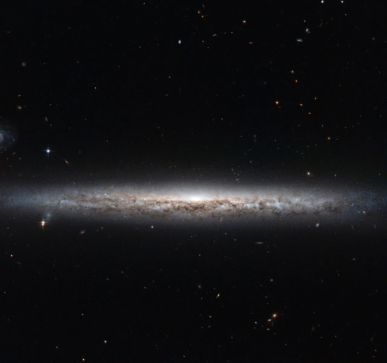 Looking into the disk of a galaxy, we see a glowing white center and billions of stars, with streaks of reddish-brown gas and dust. All against the black backdrop of space.