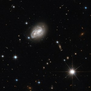 Two spiral galaxy disks intertwining as they interact, with their cores looking like a pair of eyes, against a black backdrop of other galaxies.