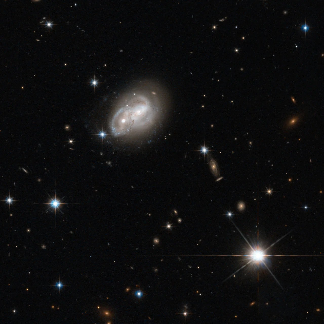 Two spiral galaxy disks intertwining as they interact, with their cores looking like a pair of eyes, against a black backdrop of other galaxies.