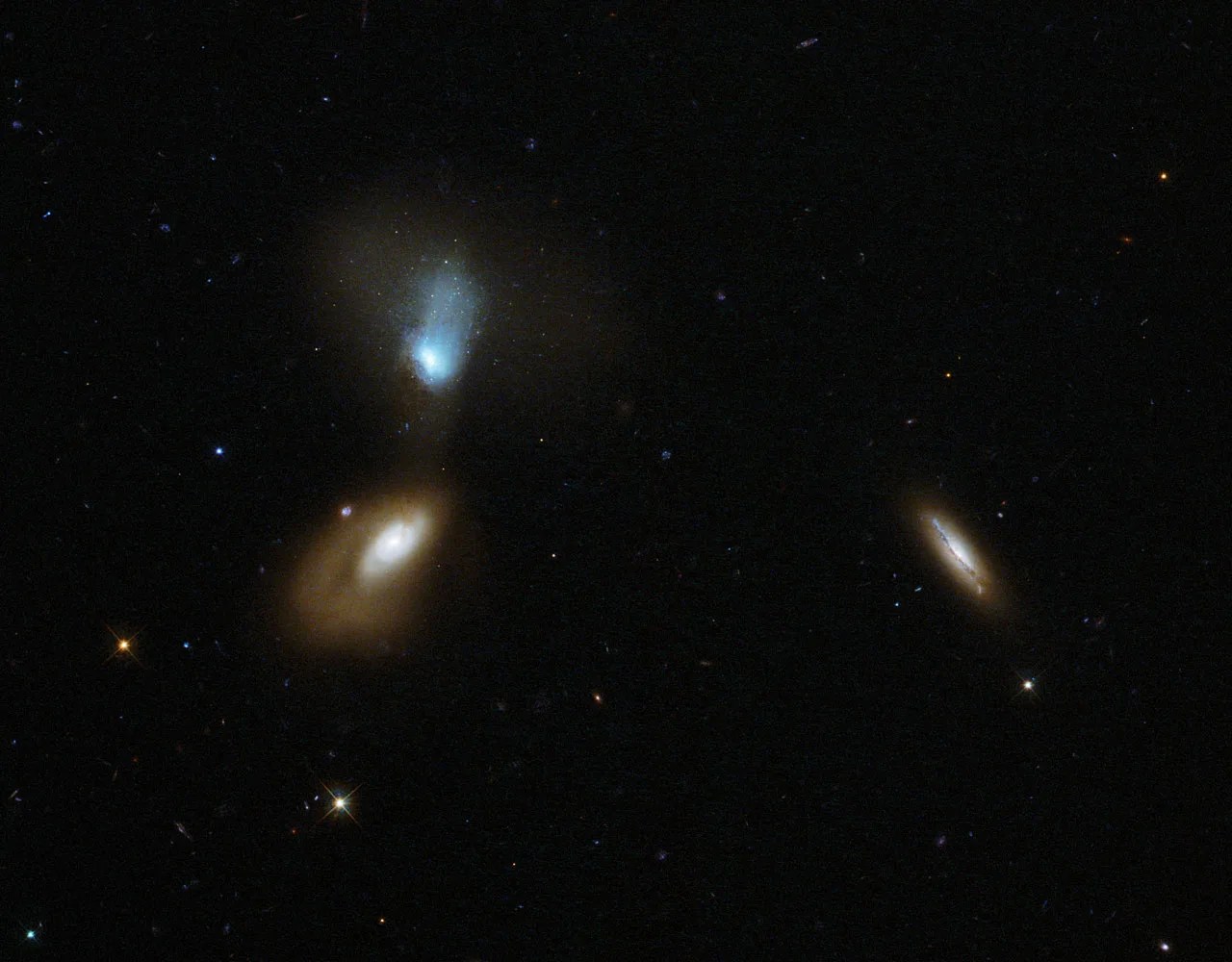 Three galaxies - two of which are on the left and are relatively close in the picture, visibly distorting each other. The third galaxy is on the right side of the image.