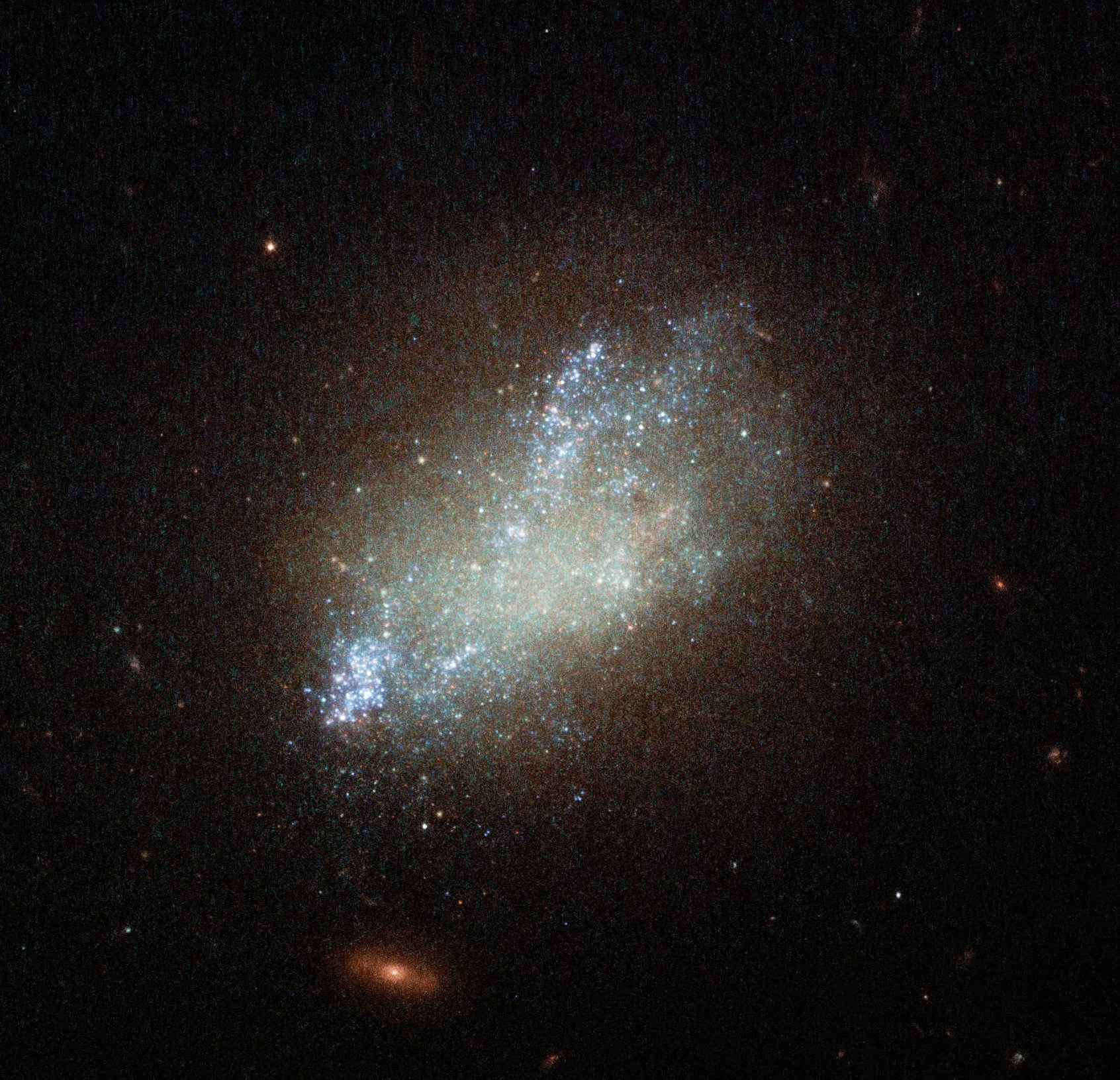A cloudy smudge of stars with a very small orange background galaxy below it.