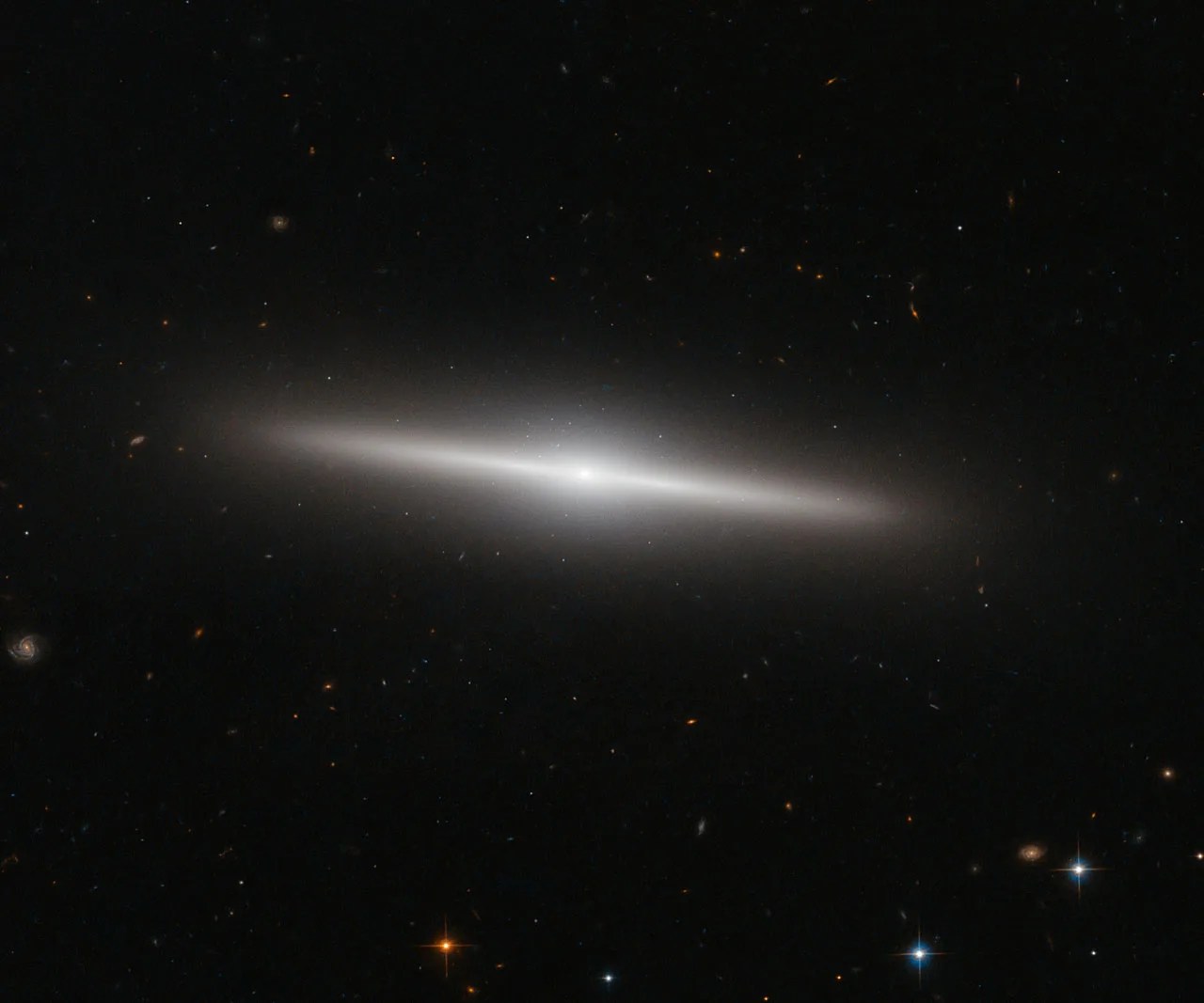 A delicate side-on galaxy in a field of black. The core is visible as a brighter spot in the center and the galaxy itself is tilted so it appears almost as a thin white glowing line.