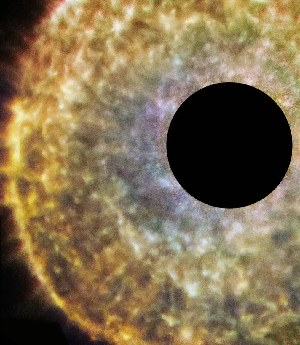 A large black dot obscures the center of the star in order to more clearly show the area around it. A bright round region of rippled, flaring orange and yellow material, bluish toward the center, fills the frame and travels off it to the top, bottom and right.