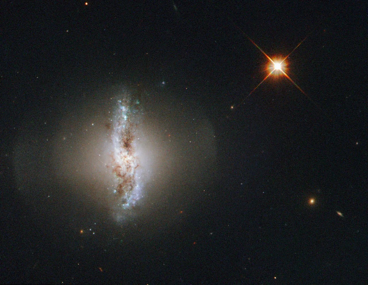 A warped looking galaxy surrounded by a round, spotlight-like glow. A bright star is to the right.