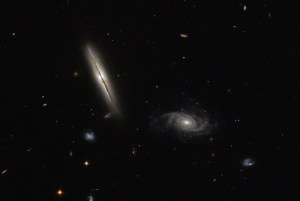 Two spiral galaxies: the main one on the left is seen nearly head-on, just able to see the brownish dust of the disk with a yellowish glow. Its companion spiral is seen more face-on, with grayish-yellow spiral arms.
