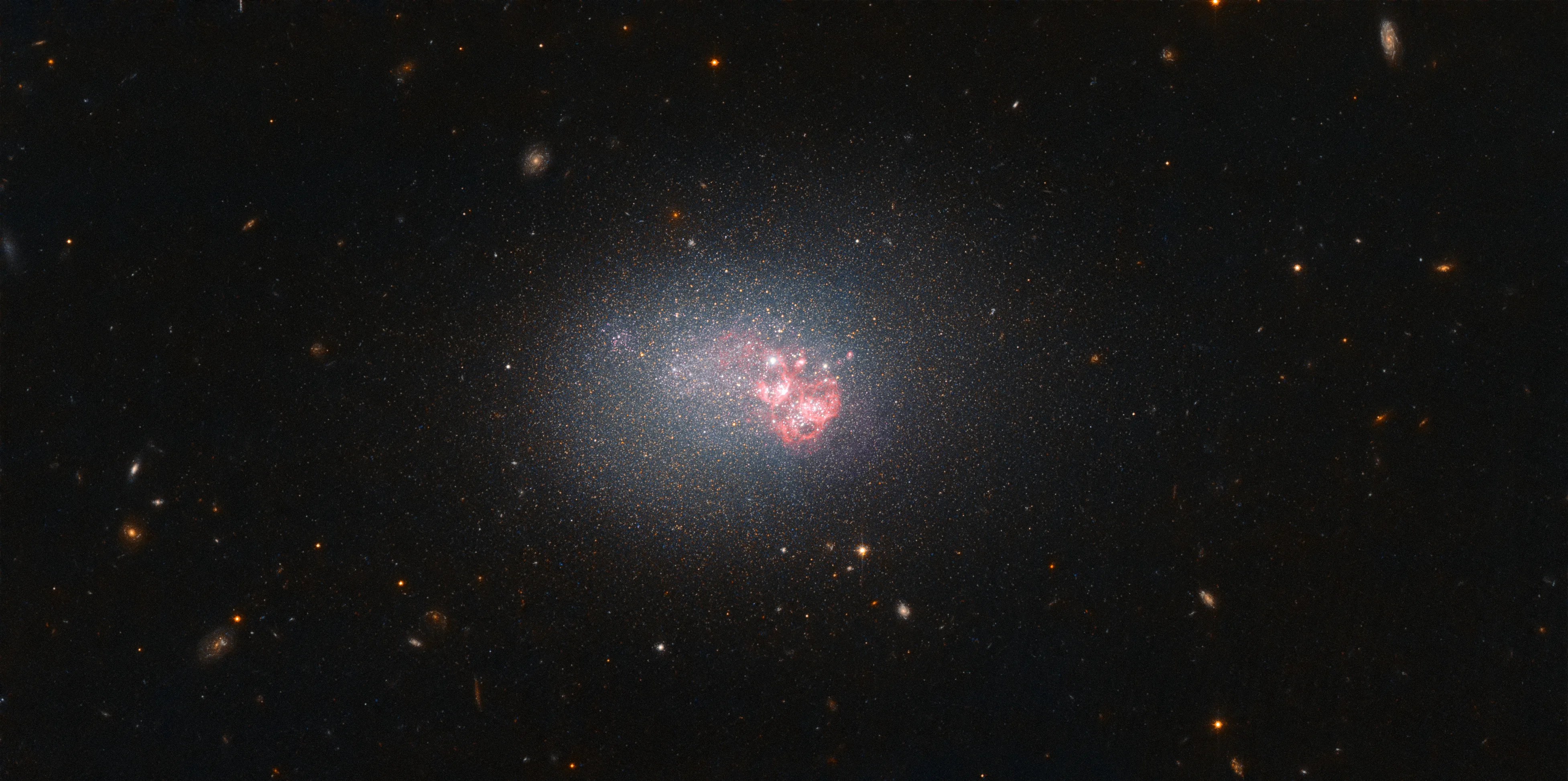 Diffuse bluish galaxy with a bright pink region off center