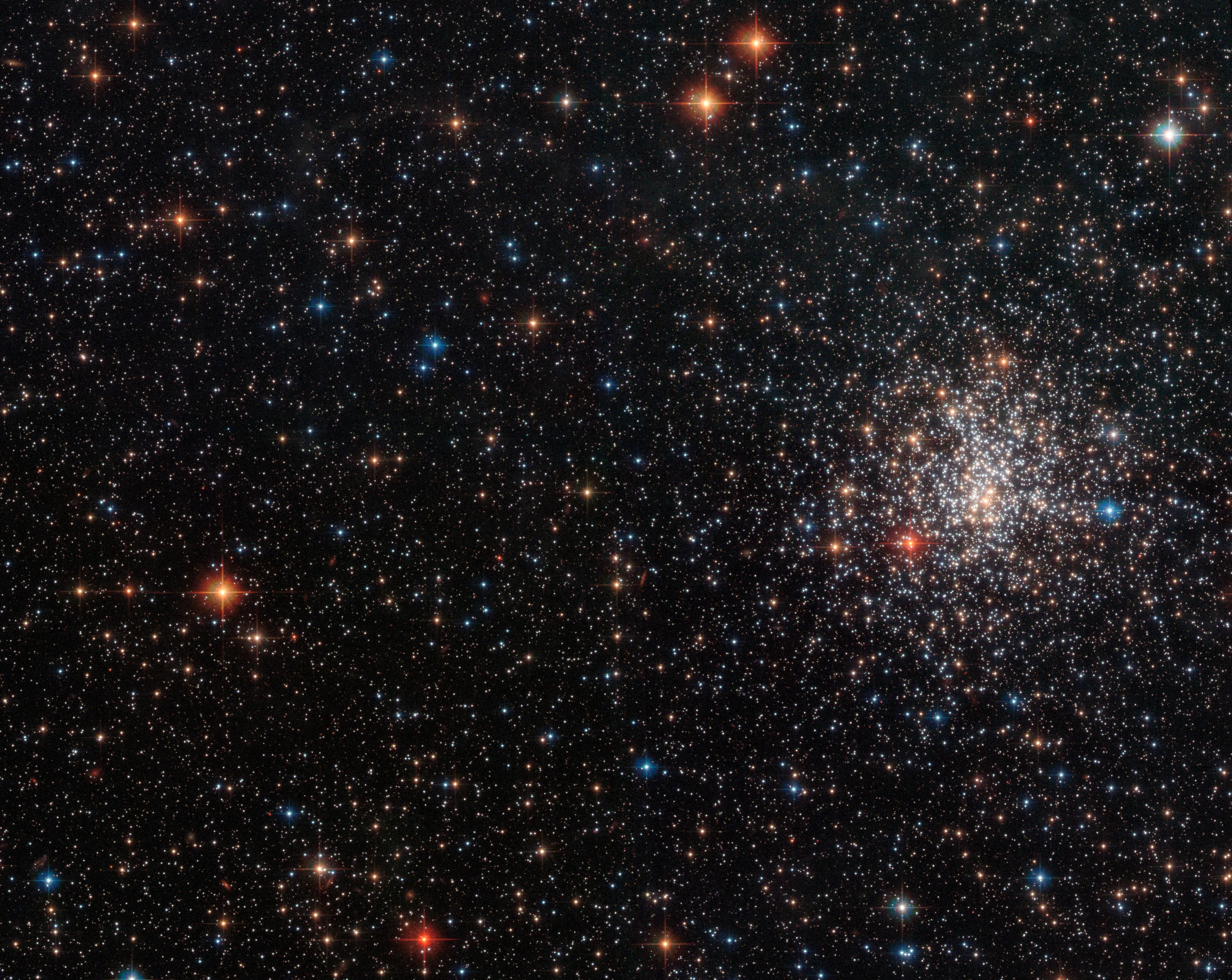 A bright cluster of stars to the right, with bright red and blue standouts