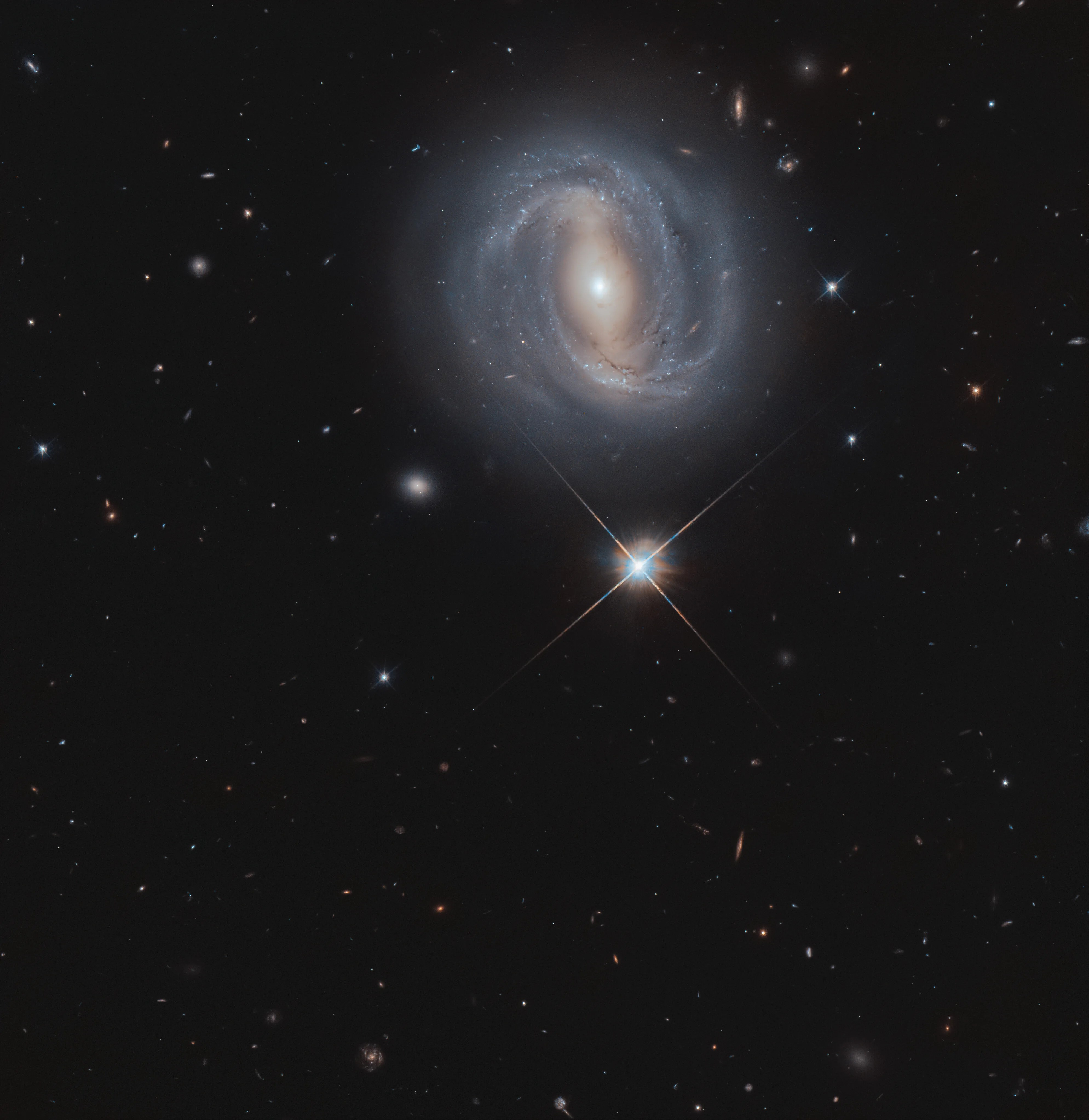 Bright spiral galaxy appearing above a bright star against the black background of space