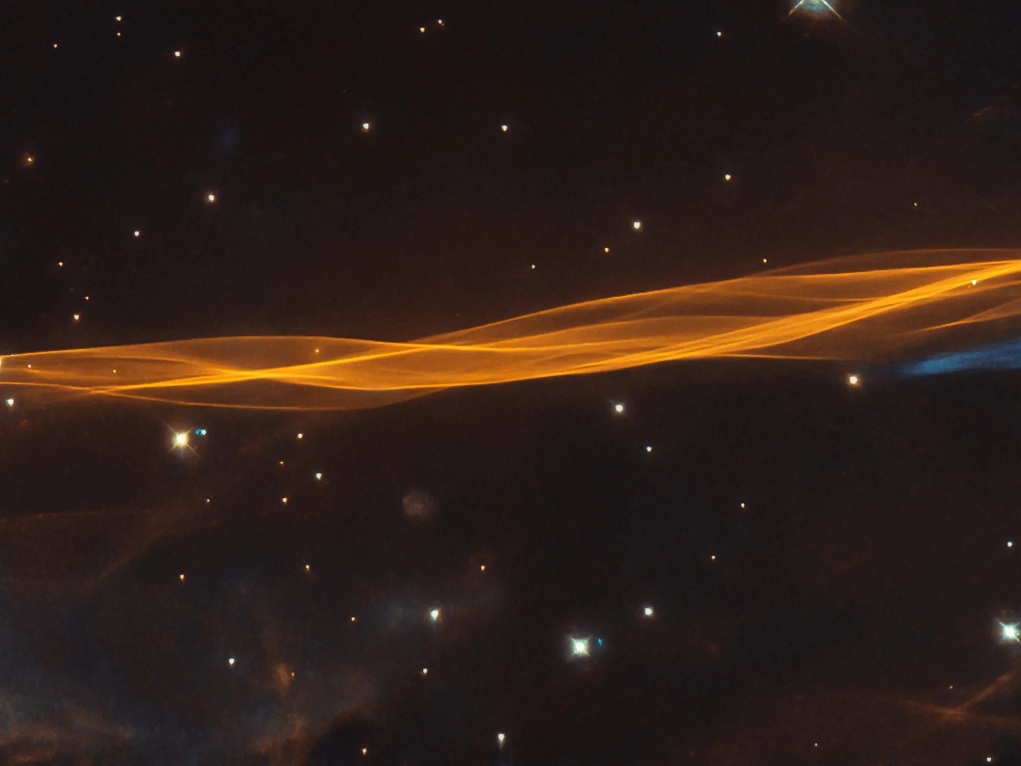 Gold-hued, veil-like strands against black backdrop of space: a small section of cygnus supernova blast wave as seen by hubble