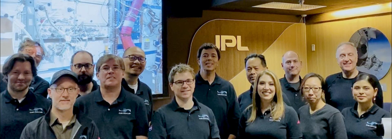 Photo of group of researchers and scientists standing in front of a monitor and JPL sign