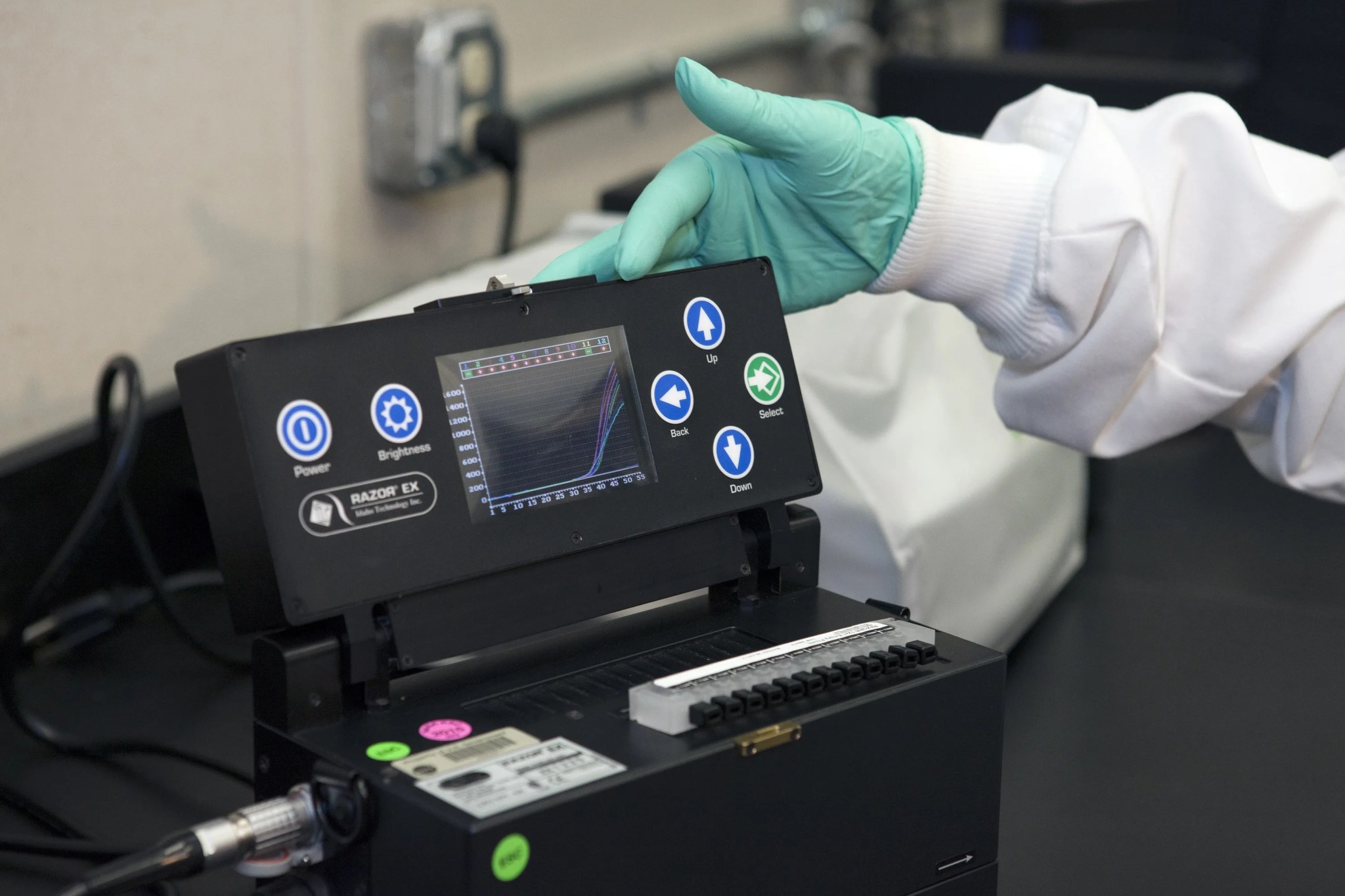 Scientist's hand pointing to display on black test equipment.